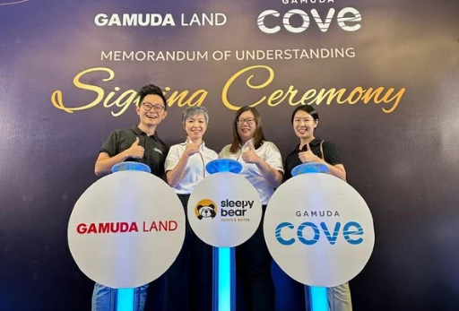MoU of Sleepy Bear Group. Four people standing behind two circular signs with logos: one for Gamuda Land and one for Gamuda Cove, at a signing ceremony for a memorandum of understanding.