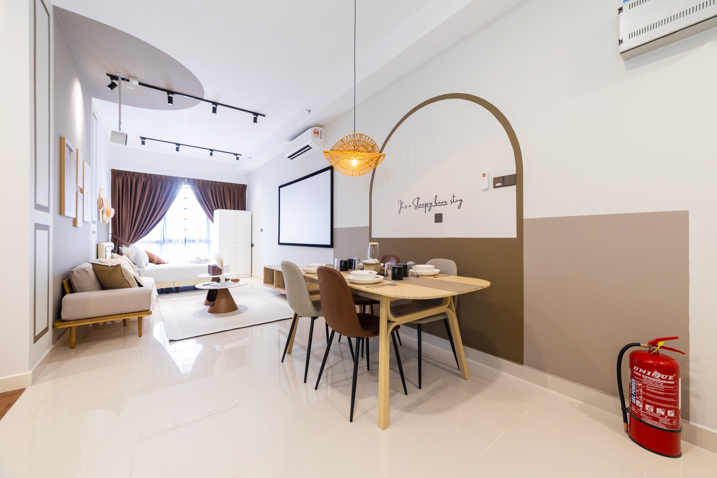 Interior of a modern living room and dining area with beige and white furniture, wall art, a large window with brown curtains, a decorative light fixture, and a fire extinguisher on the floor.