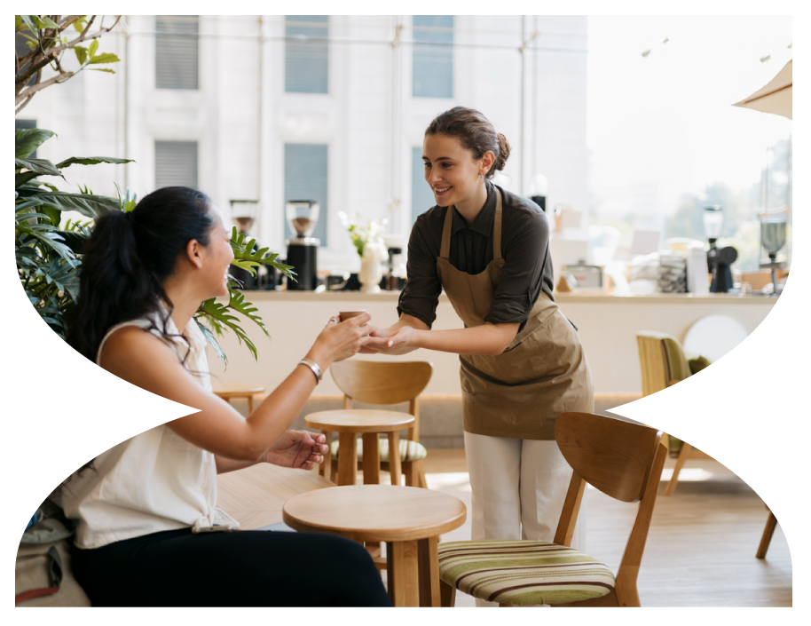 A waitress taking an order from a woman sitting at a table in a well-lit cafe.