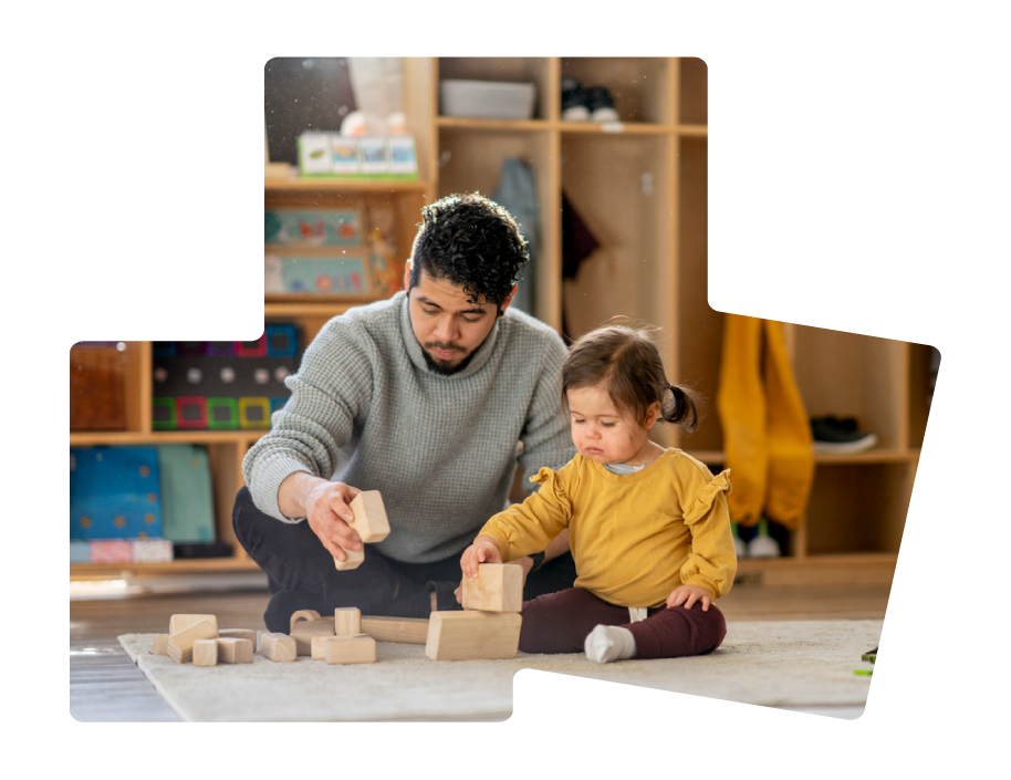 A man and young girl playing with wooden blocks on a rug in a playroom with shelves in the background.