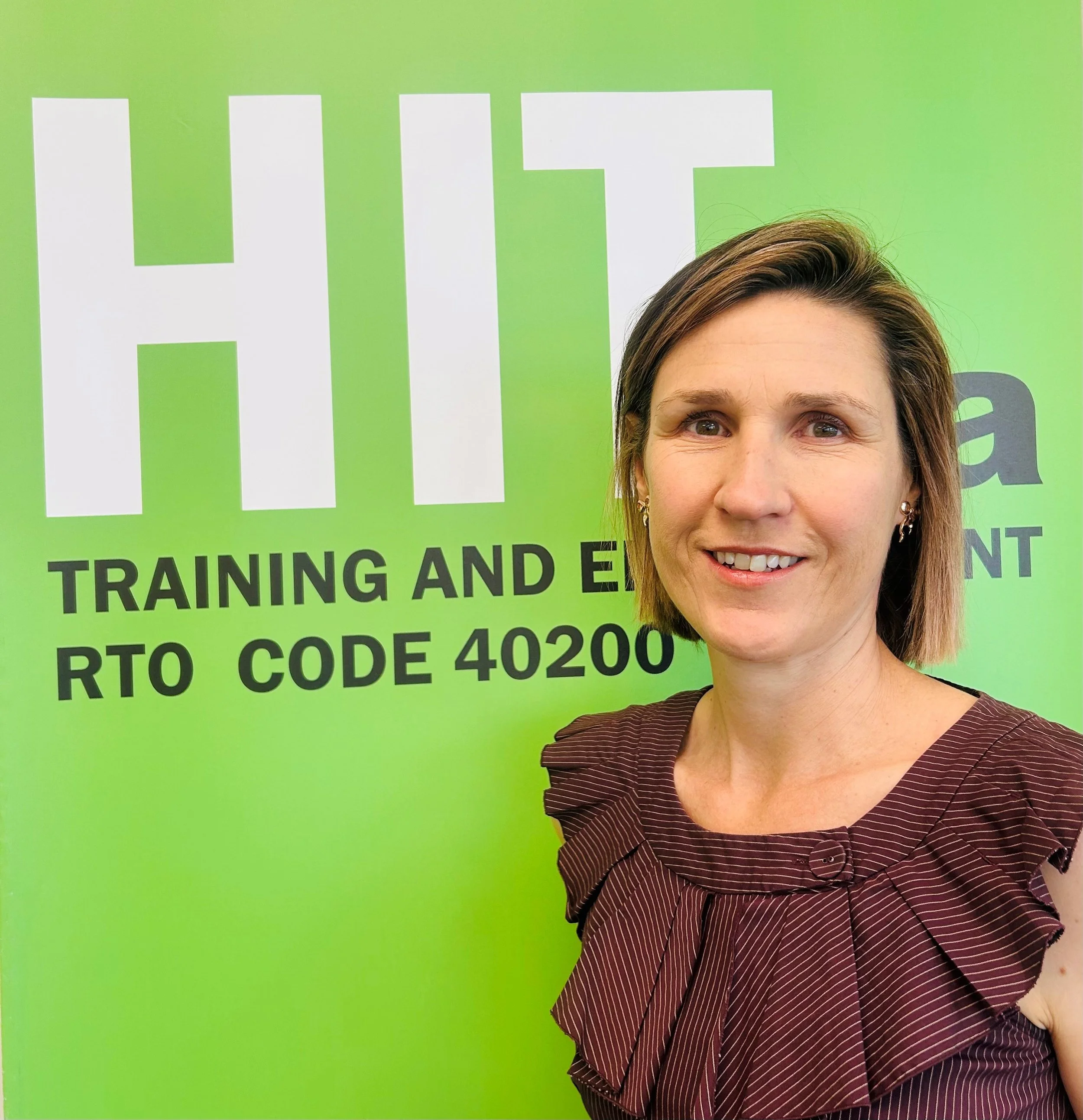 Close-up of a woman smiling, with a bright green sign in the background that has large white and black text.
