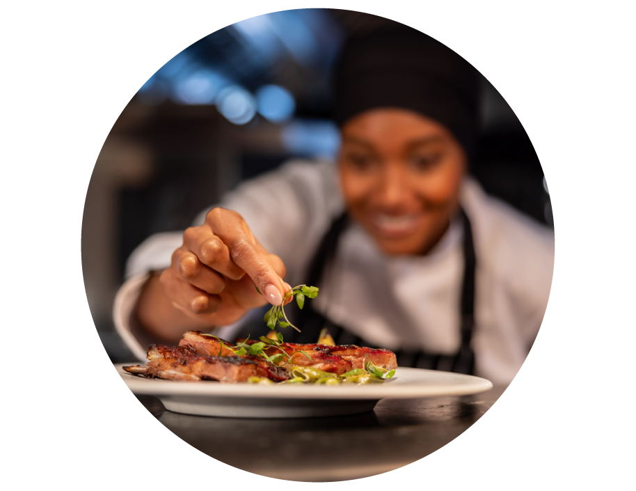 Chef garnishing a cooked dish with fresh herbs in a kitchen.