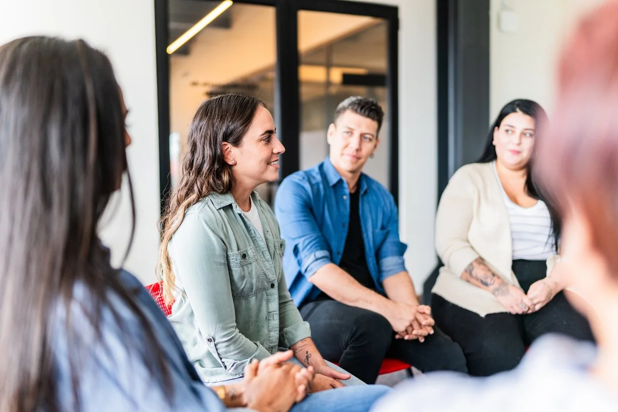 Group of diverse young adults sitting in a circle during a discussion in a modern office space.