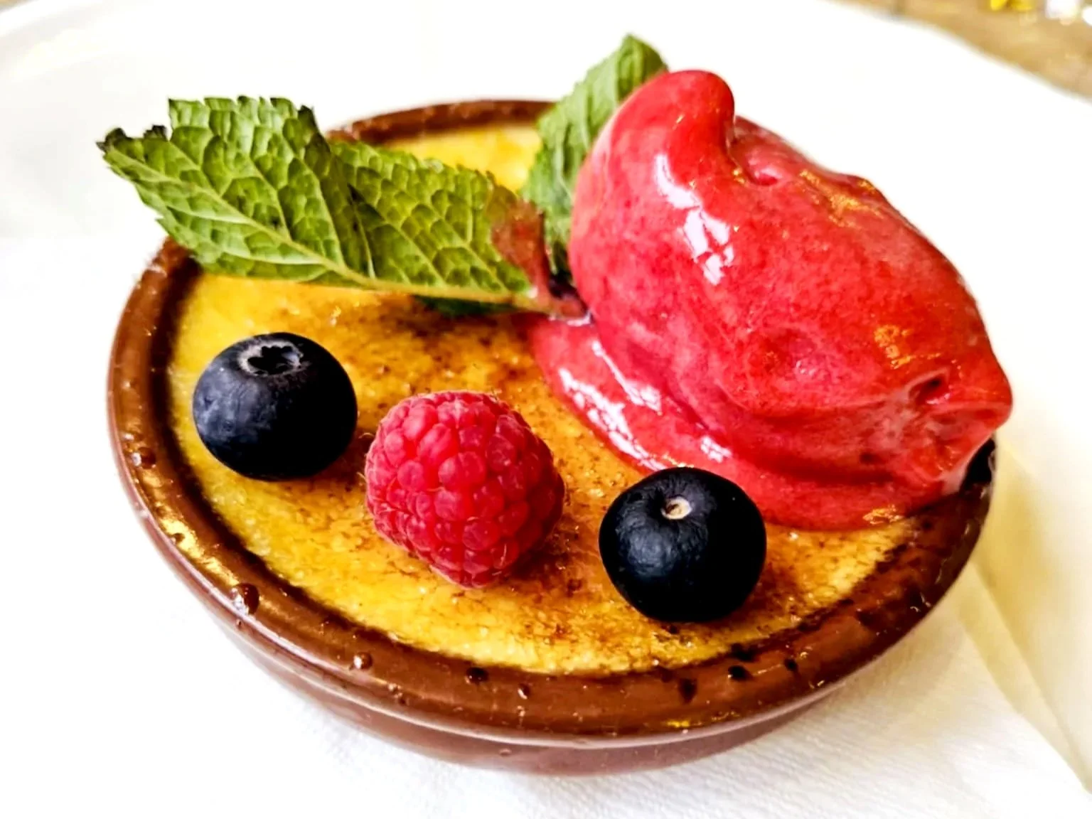 Crème brûlée pyntet med bær og mynteblade.