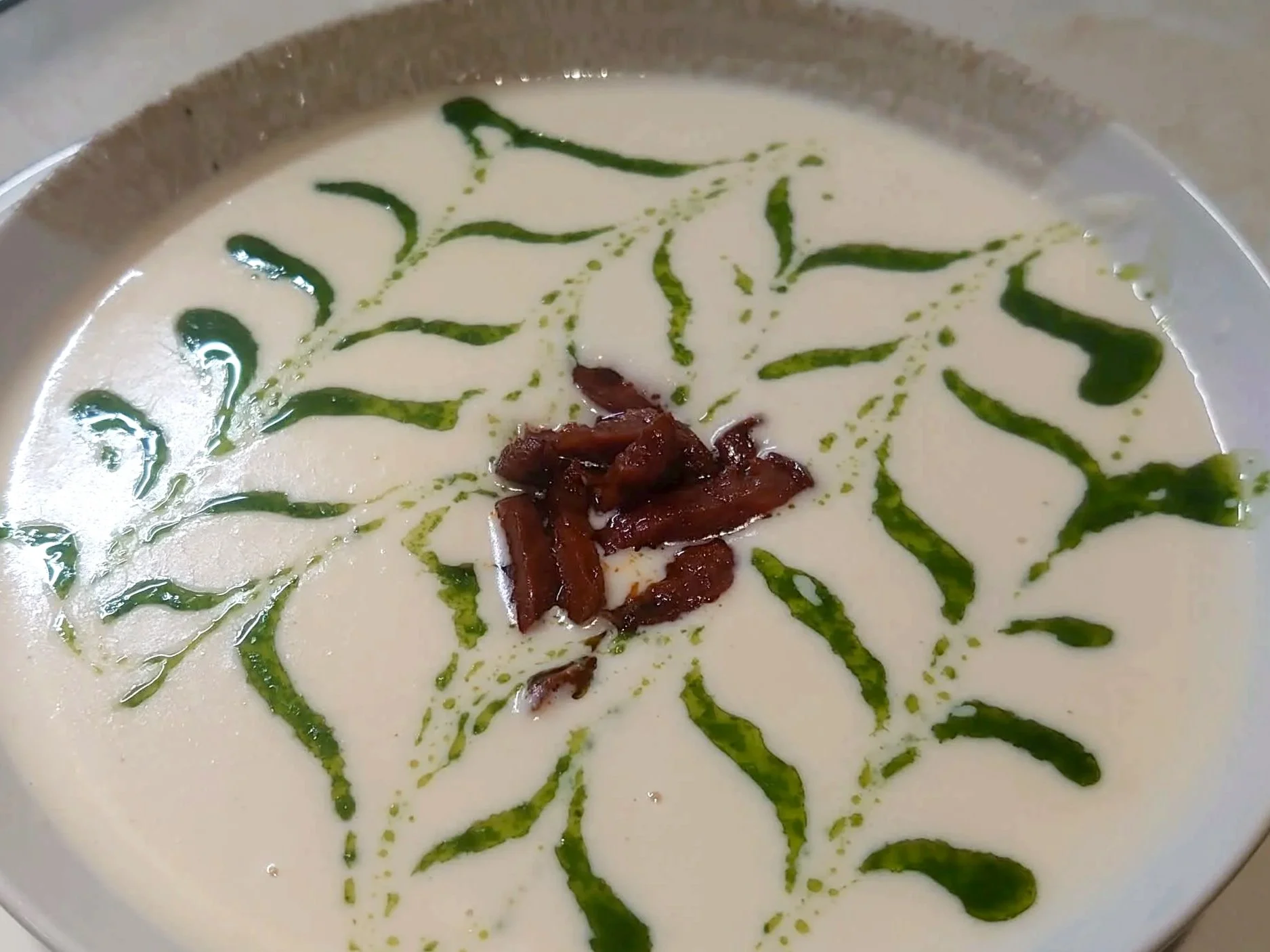 Cremet blomkålssuppe pyntet med ristet chorizo og grøn urteolie.