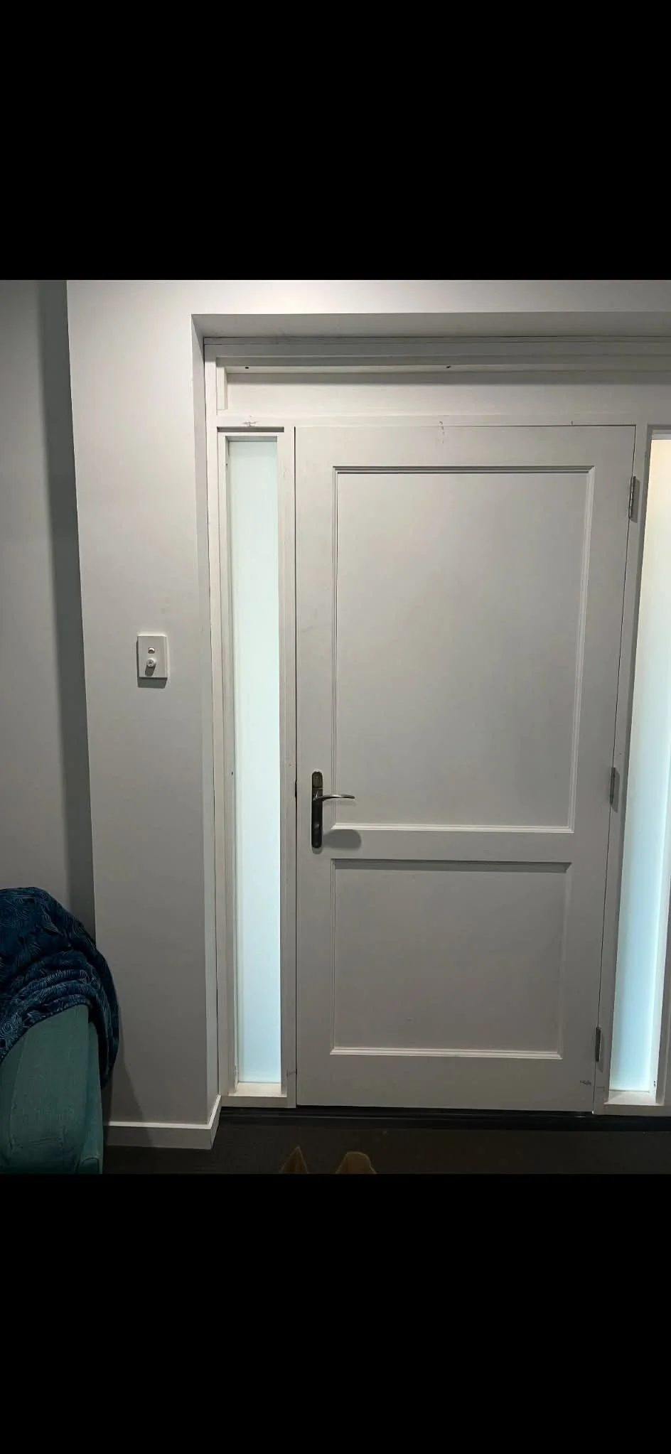 A white front door with a black handle, flanked by tall narrow windows with frosted glass, in a modern home interior.