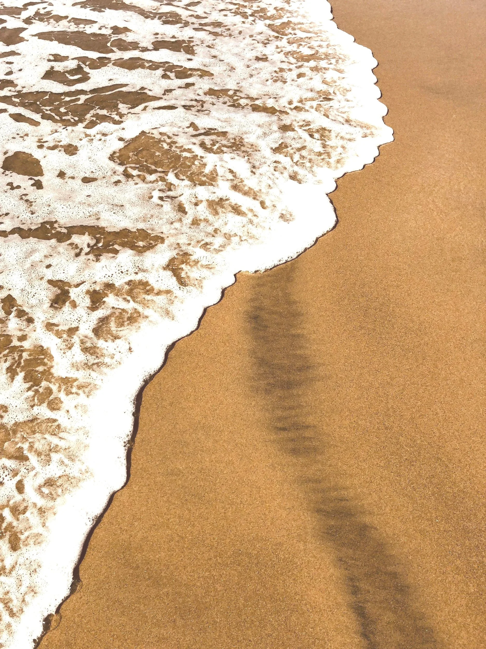 Sandstrand mit Meereswellen, die an den Strand schlagen, Wasser mit Schaum und eine klare Scheidung zwischen Wasser und Sand.