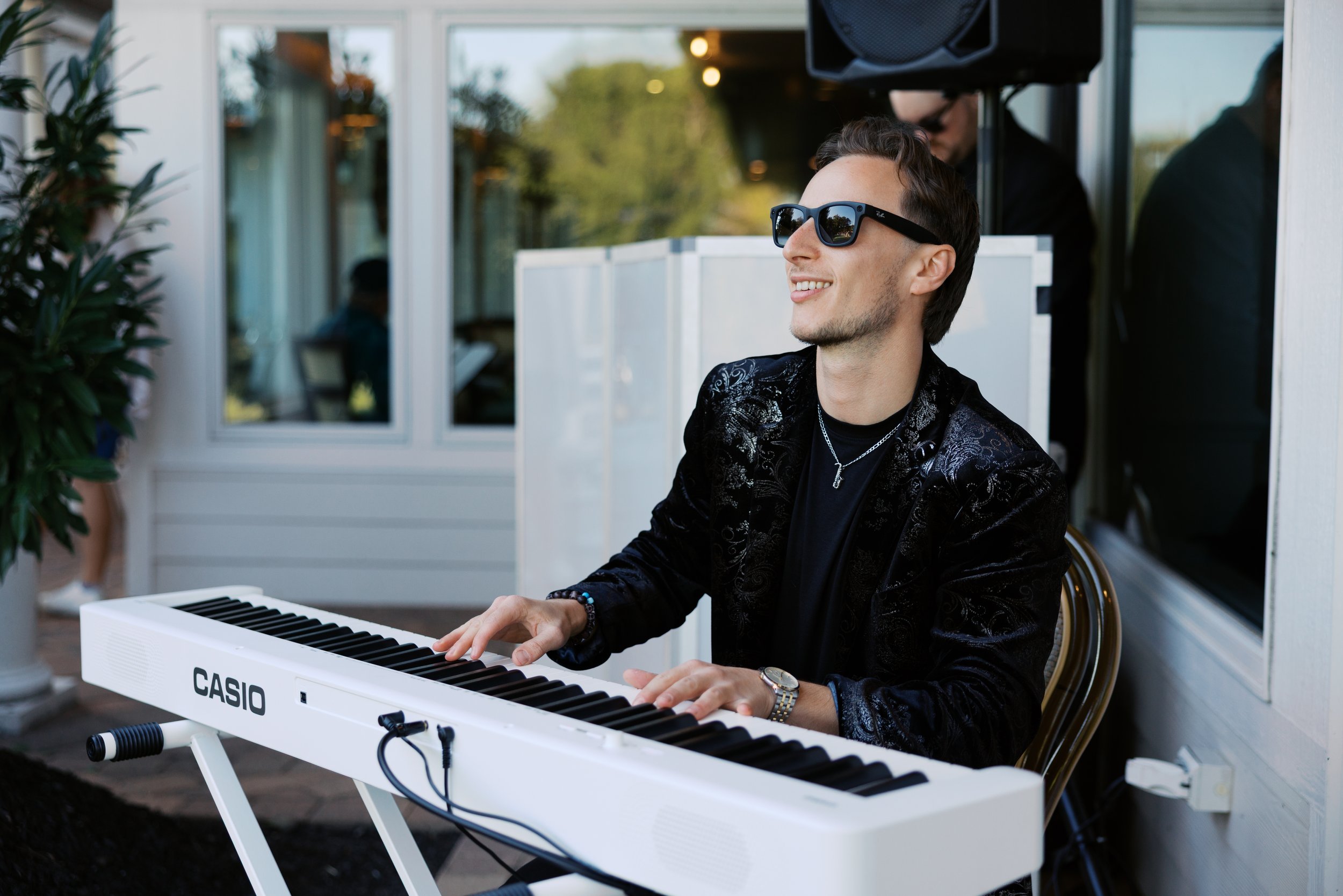 Jason Nelson wearing sunglasses playing a white Casio piano keyboard outdoors during a wedding ceremony in Charleston, South Carolina.