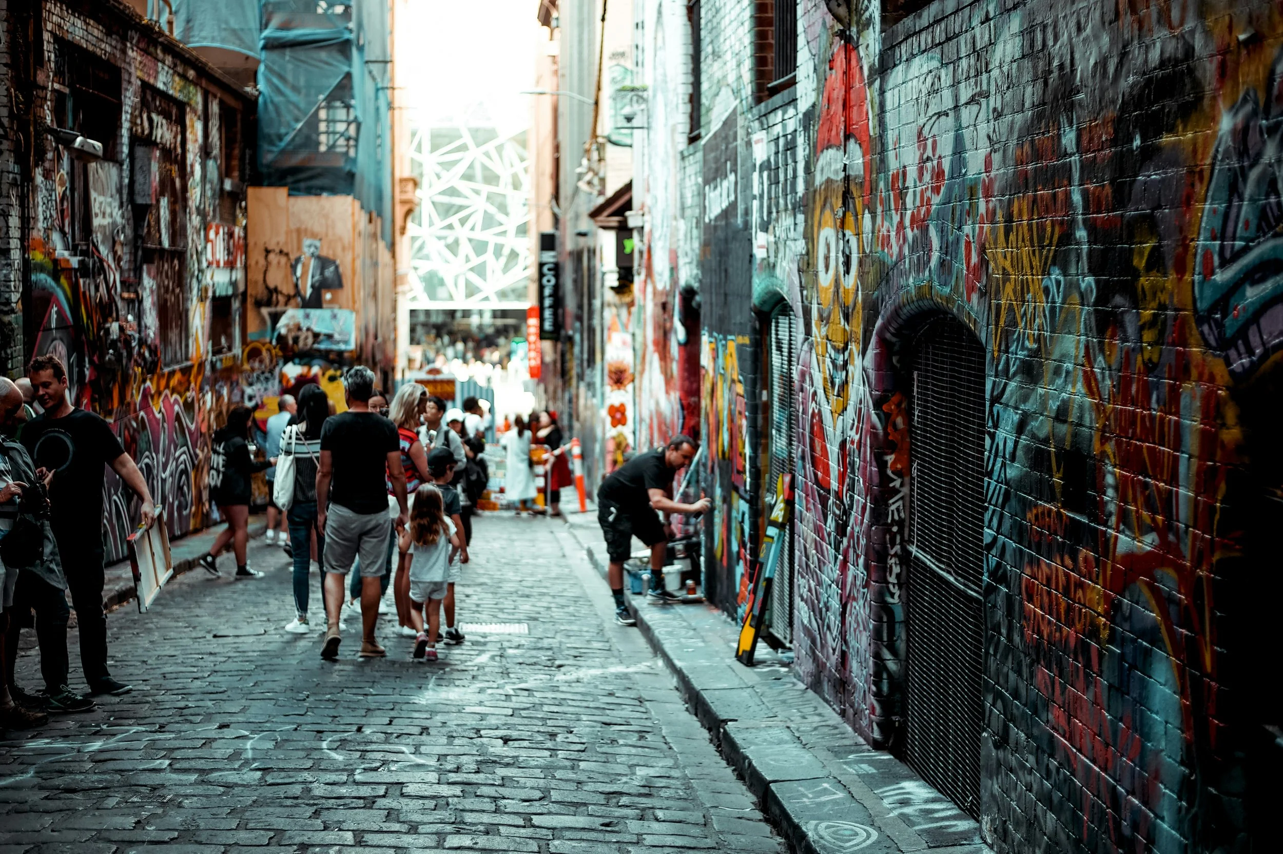 Una calle peatonal de calle con paredes cubiertas de graffiti y murales, con varias personas caminando y observando el arte urbano.