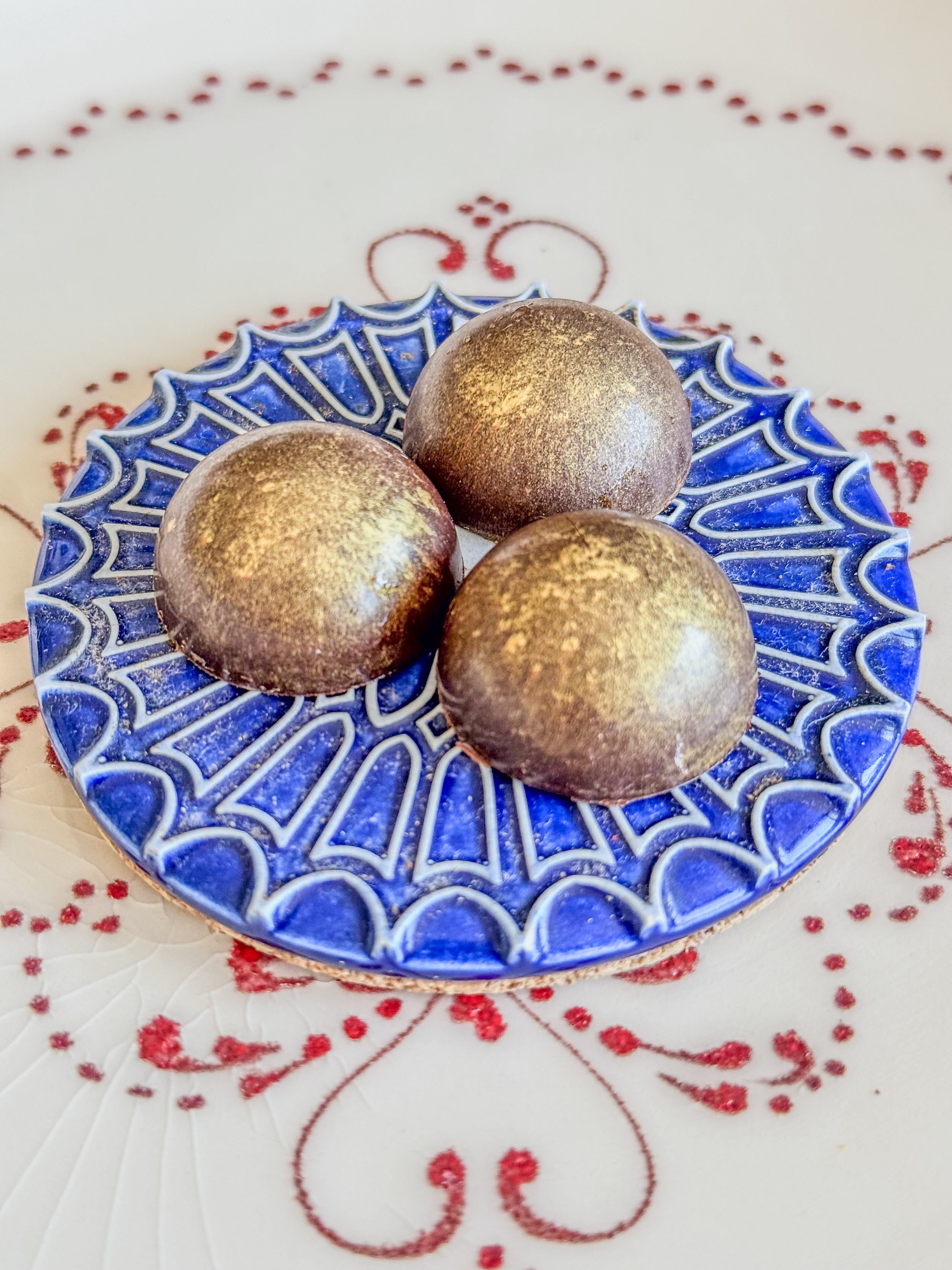 Three round chocolates with a metallic gold dust on a decorative blue and white plate.