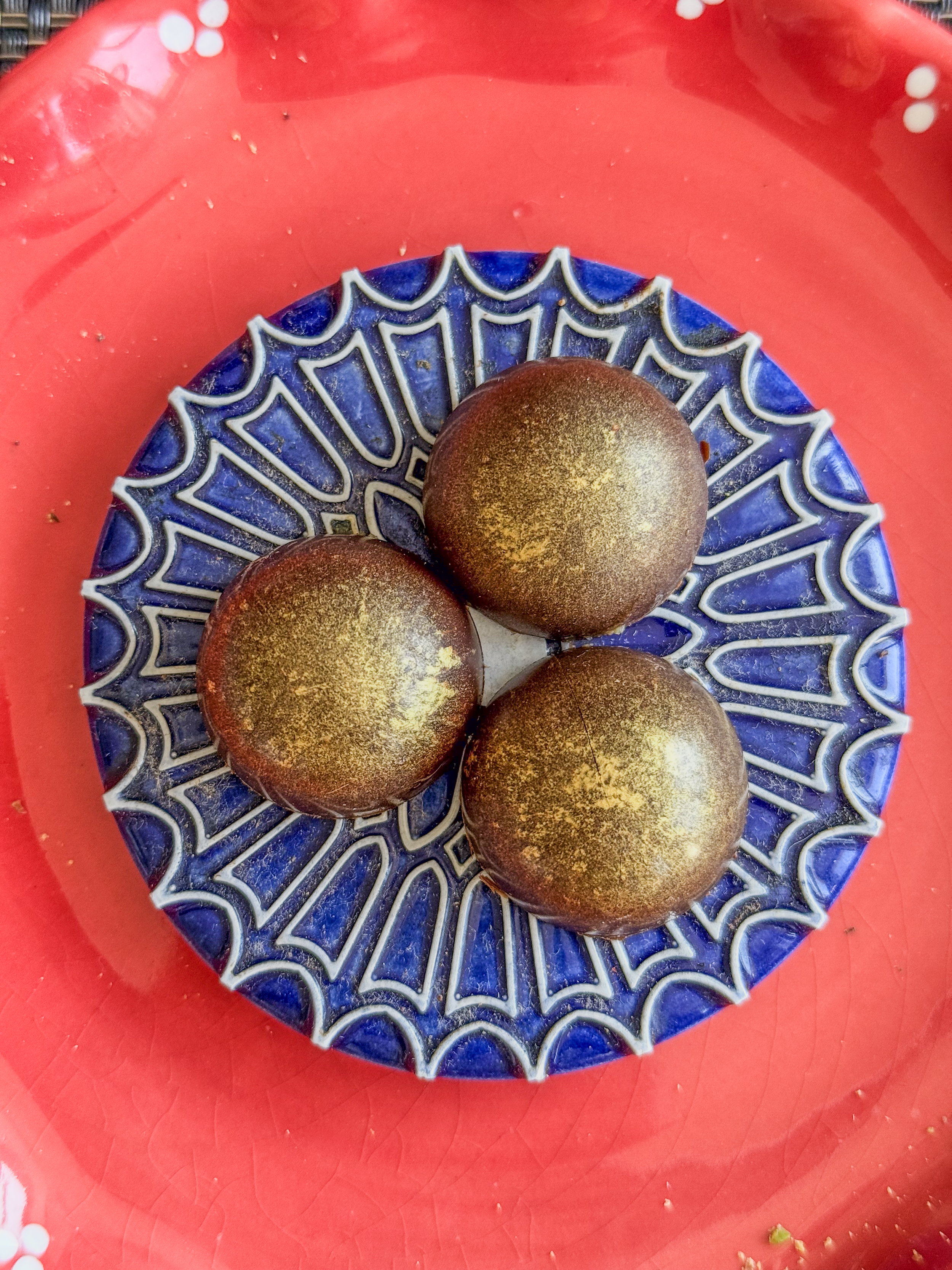 Three chocolates with gold dust on a blue and white doily on a red plate.