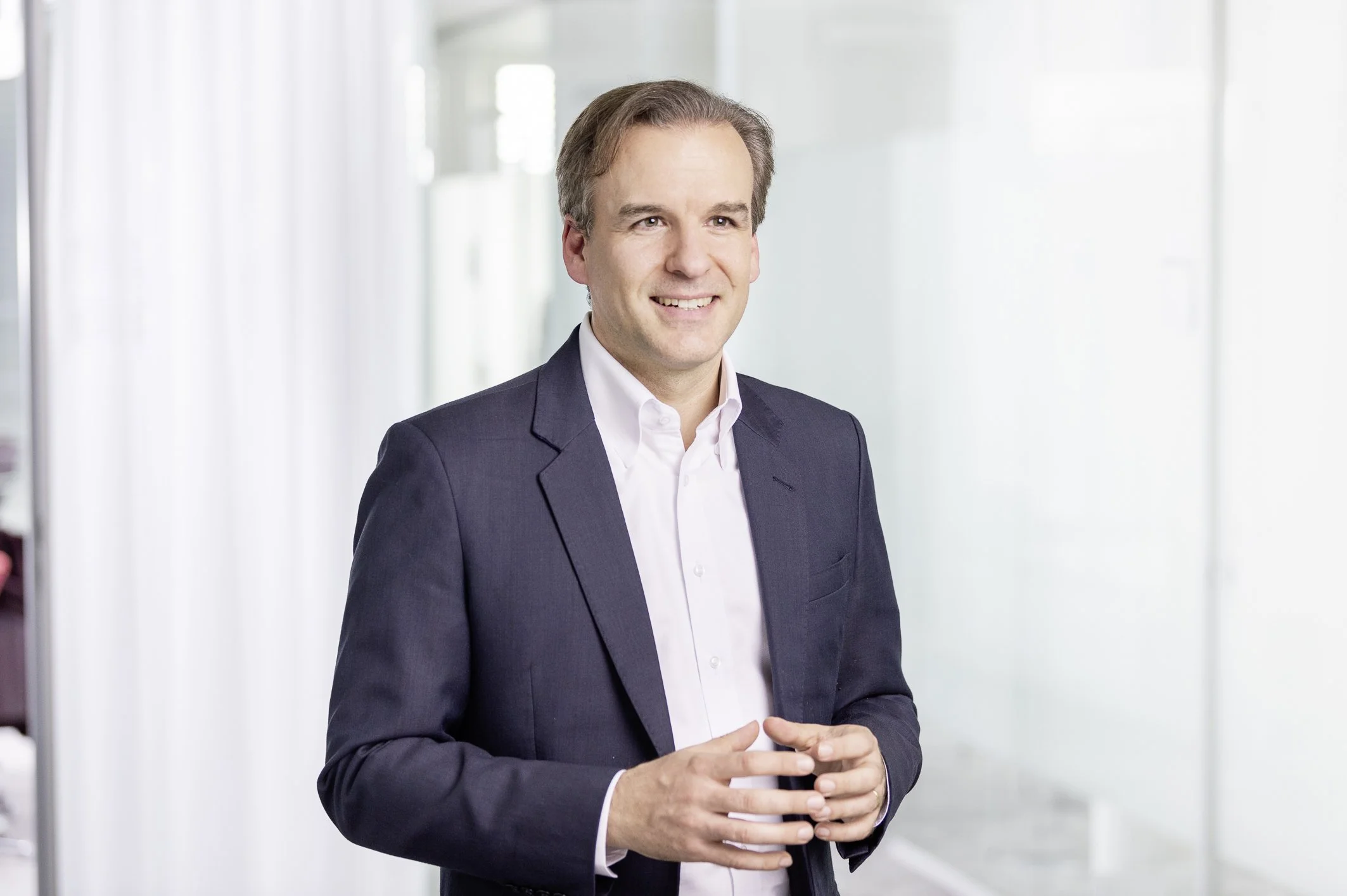 Jochen Menges standing in a dark suit jacket with his hands slightly raised.