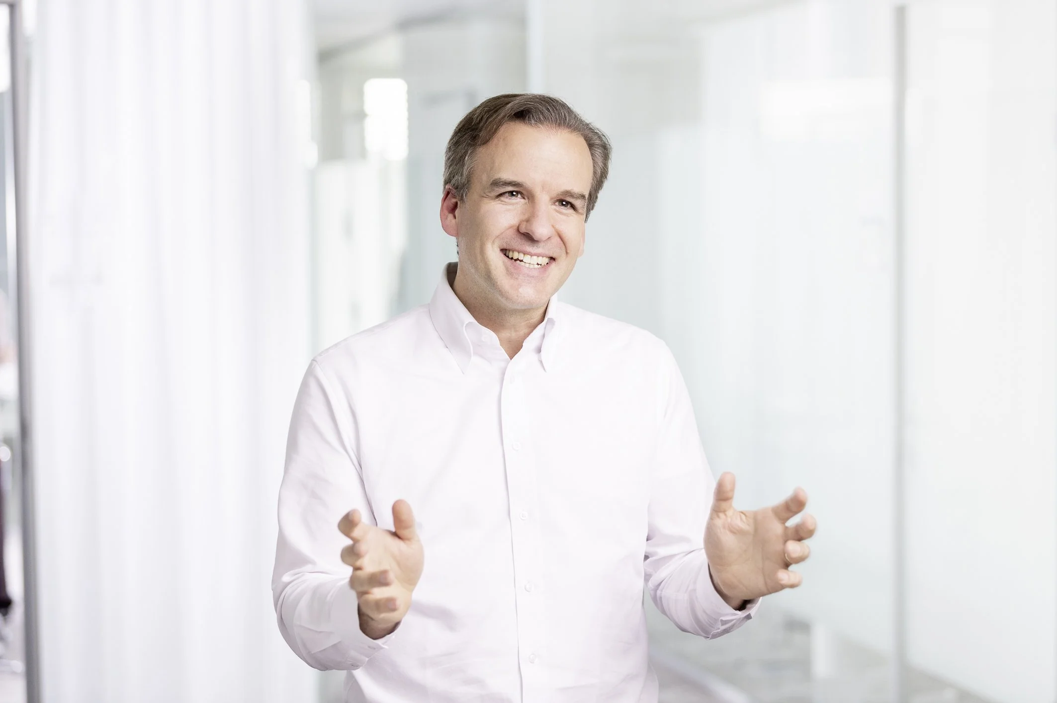 Jochen Menges smiling and gesturing with both hands in a bright office.