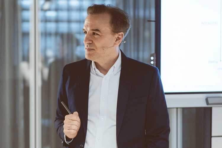Jochen Menges presenting during a professional workshop, wearing a dark suit jacket and holding a pen.