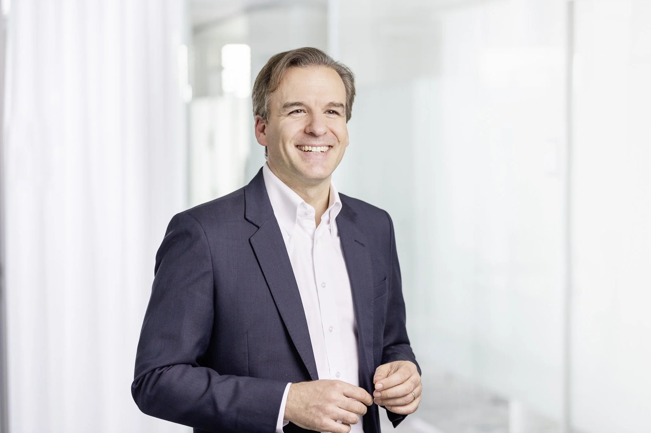 Jochen Menges smiling in a dark suit jacket against a bright office background.