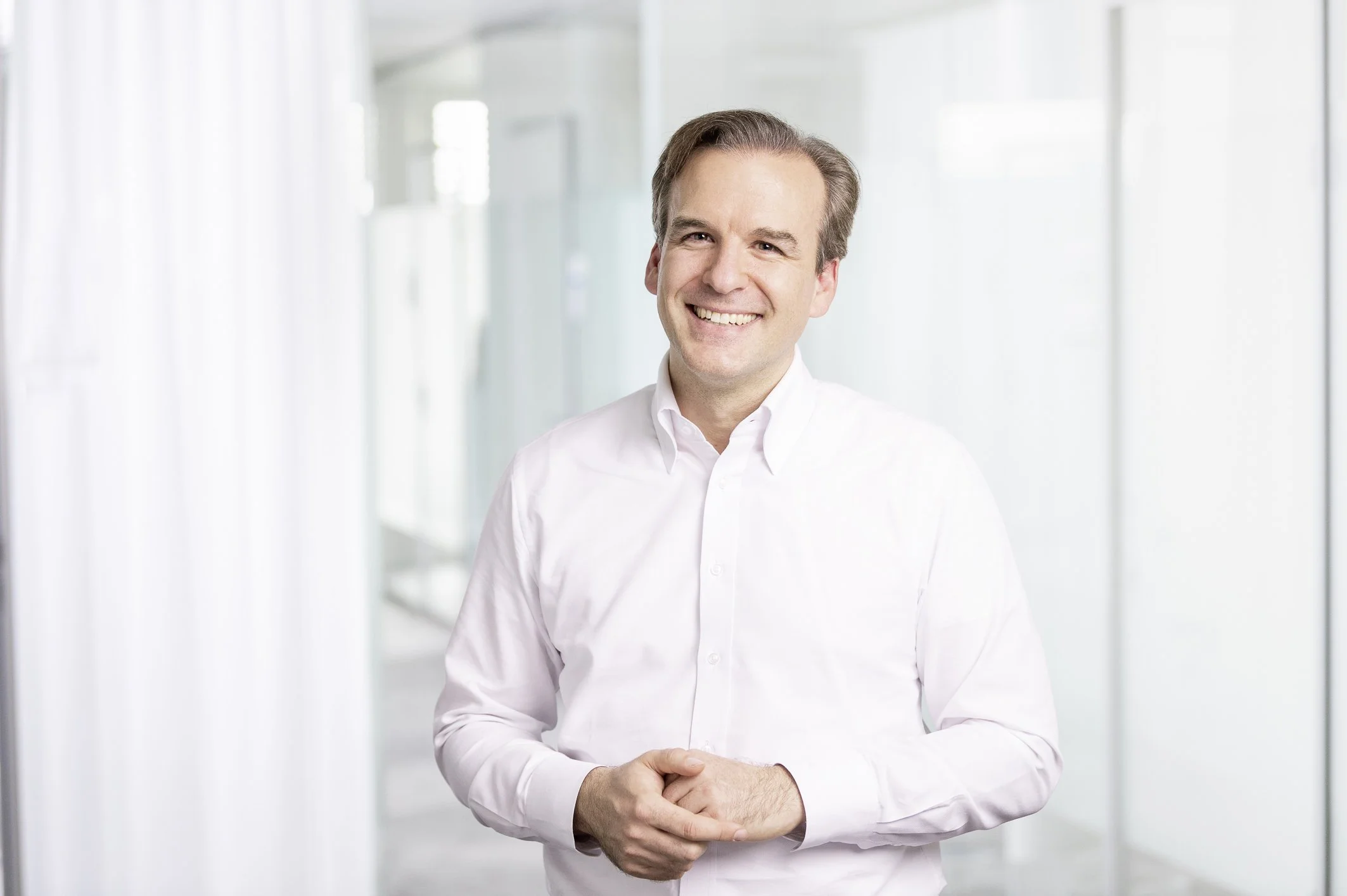 Jochen Menges smiling in a white shirt with his hands clasped.