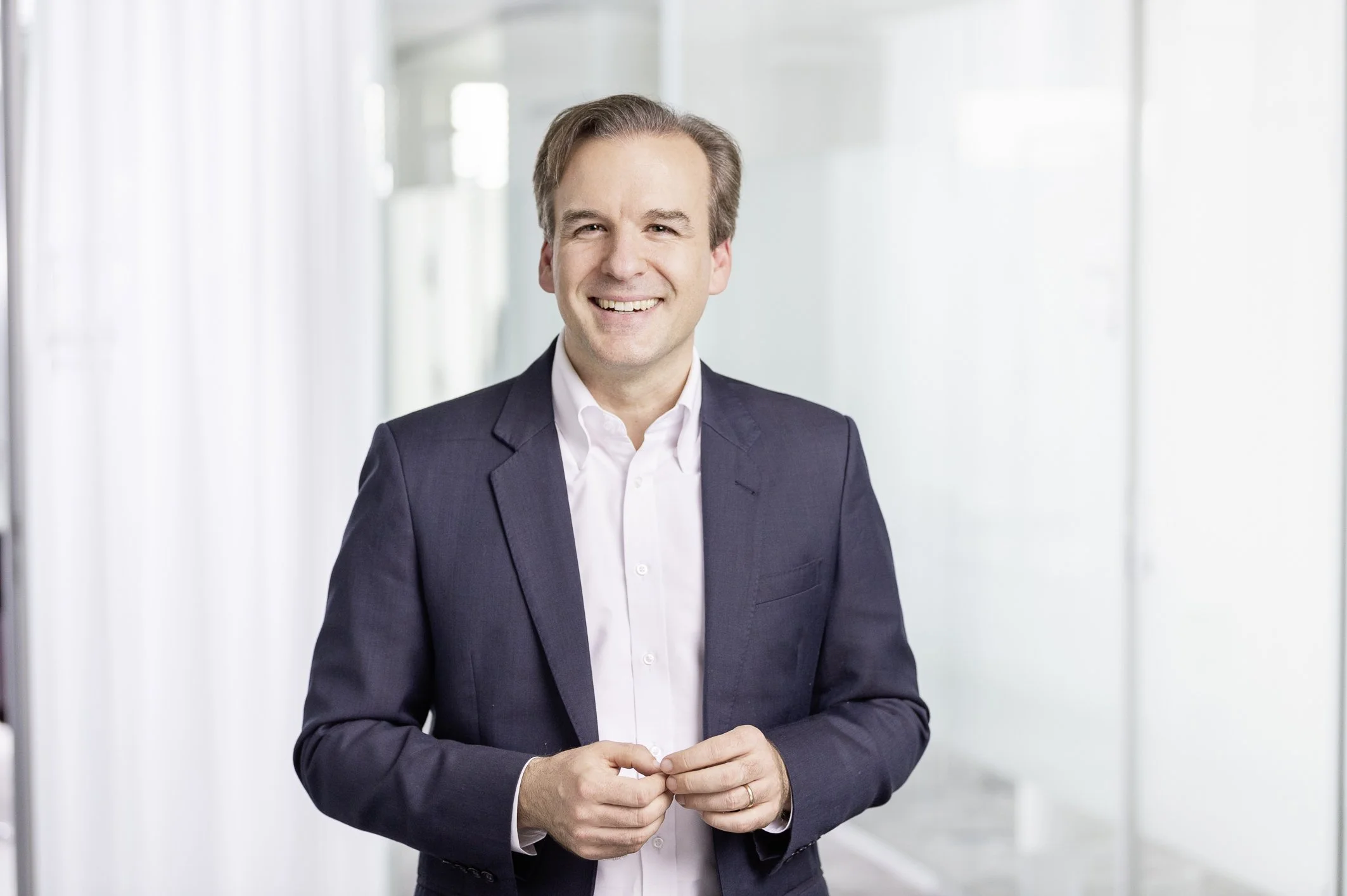 Jochen Menges smiling in a dark suit jacket and white shirt in a bright office.