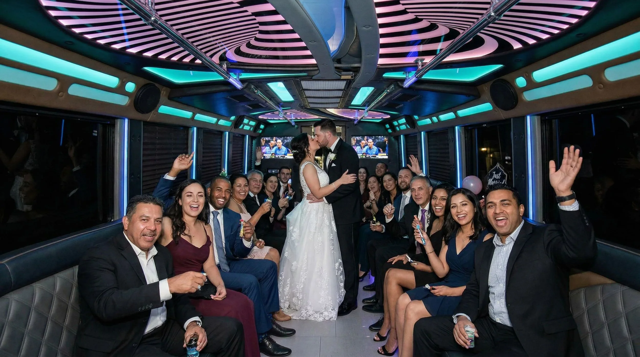 Wedding celebration inside a limousine with a bride and groom kissing, surrounded by guests cheering and smiling.