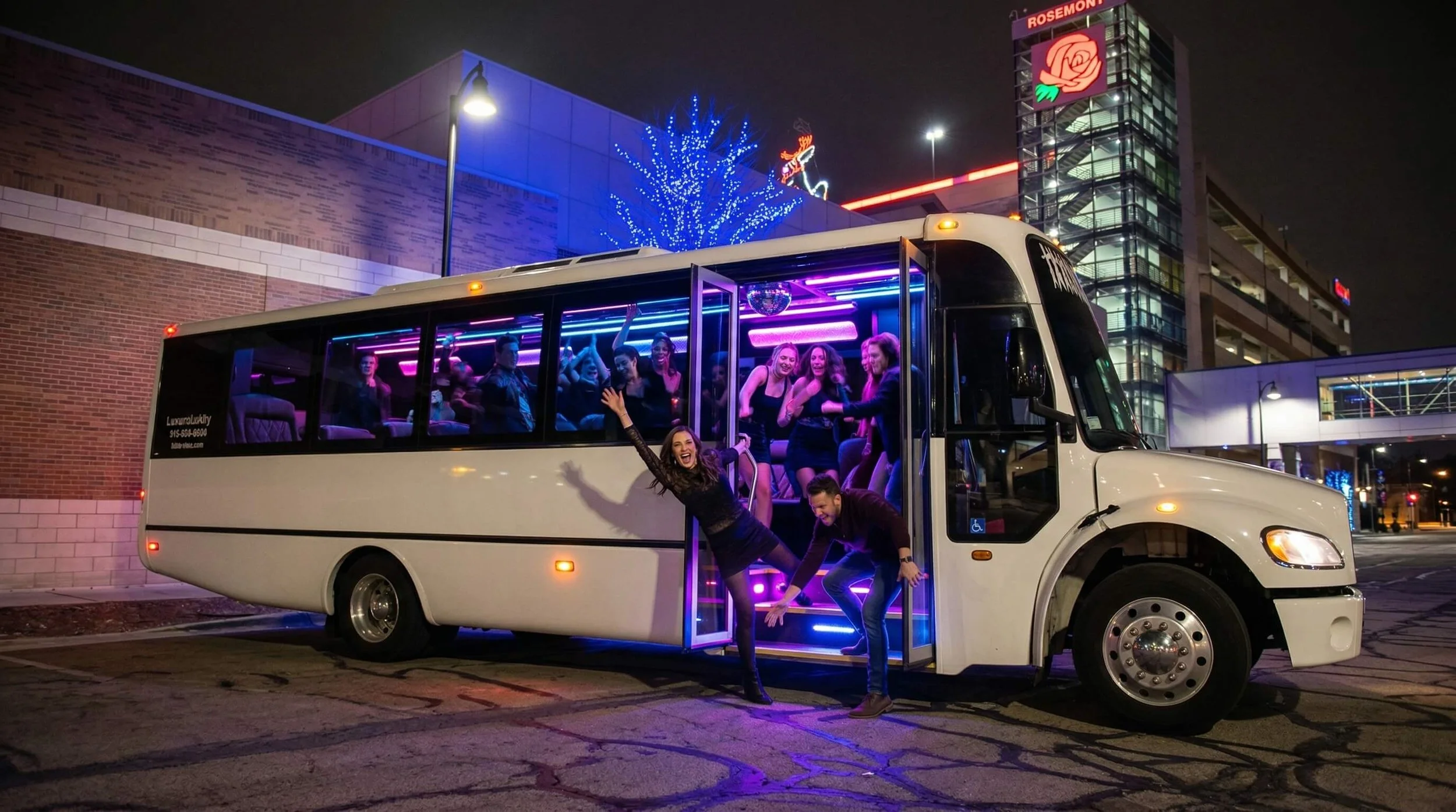 Group of people enjoying a nighttime party on a white bus with neon lights, parked in an urban area with buildings decorated with Christmas lights.
