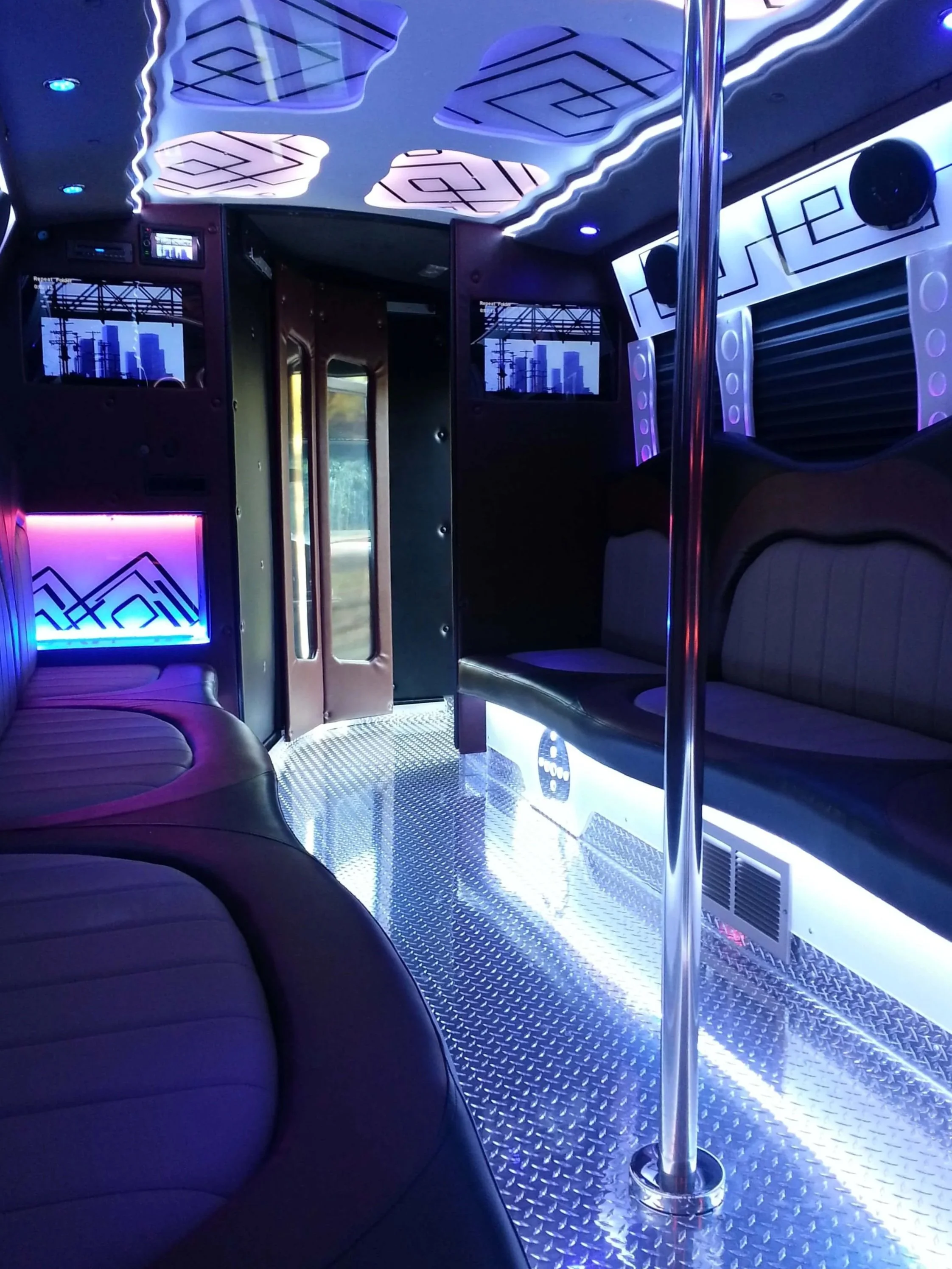 Interior of a party bus or limousine with purple and blue lighting, black leather curved seating, a shiny metallic floor, and a pole in the center.