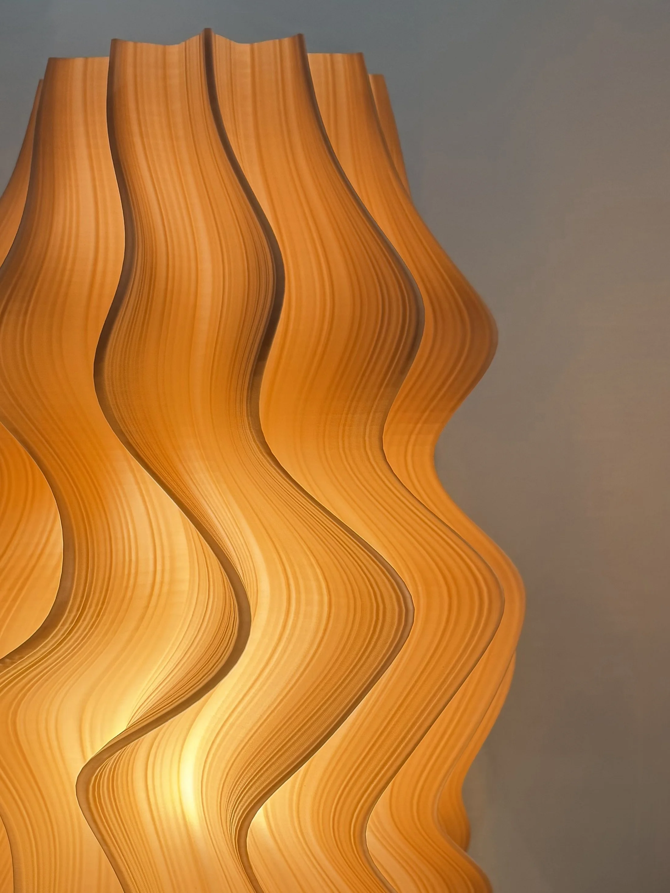 Close-up of a modern, orange, wavy pendant lamp with layered, curved panels against a plain background.