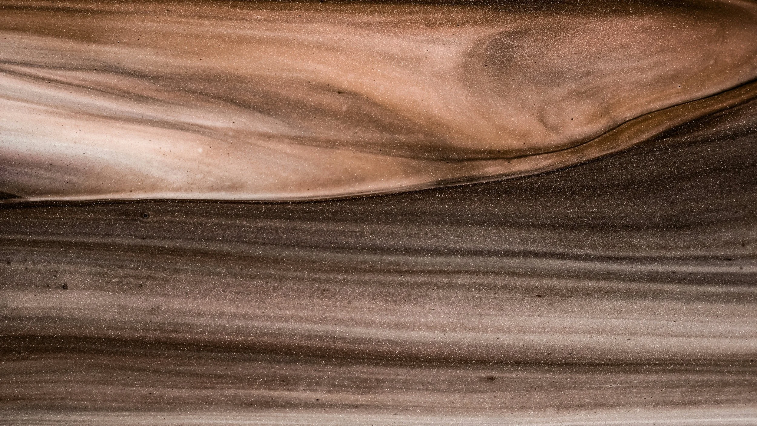Close-up of a detailed, swirling pattern of beige, brown, and tan layered sand or sediment.