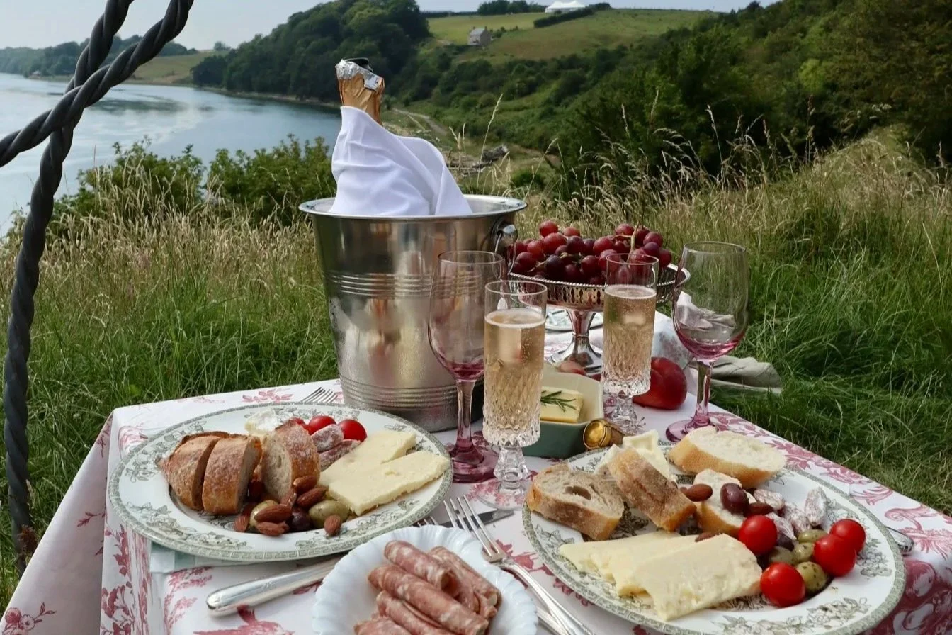 Luxury riverside picnic by Laura Somborn featuring artisan food, heritage tableware and champagne overlooking the River Tweed near the Royal Border Bridge.