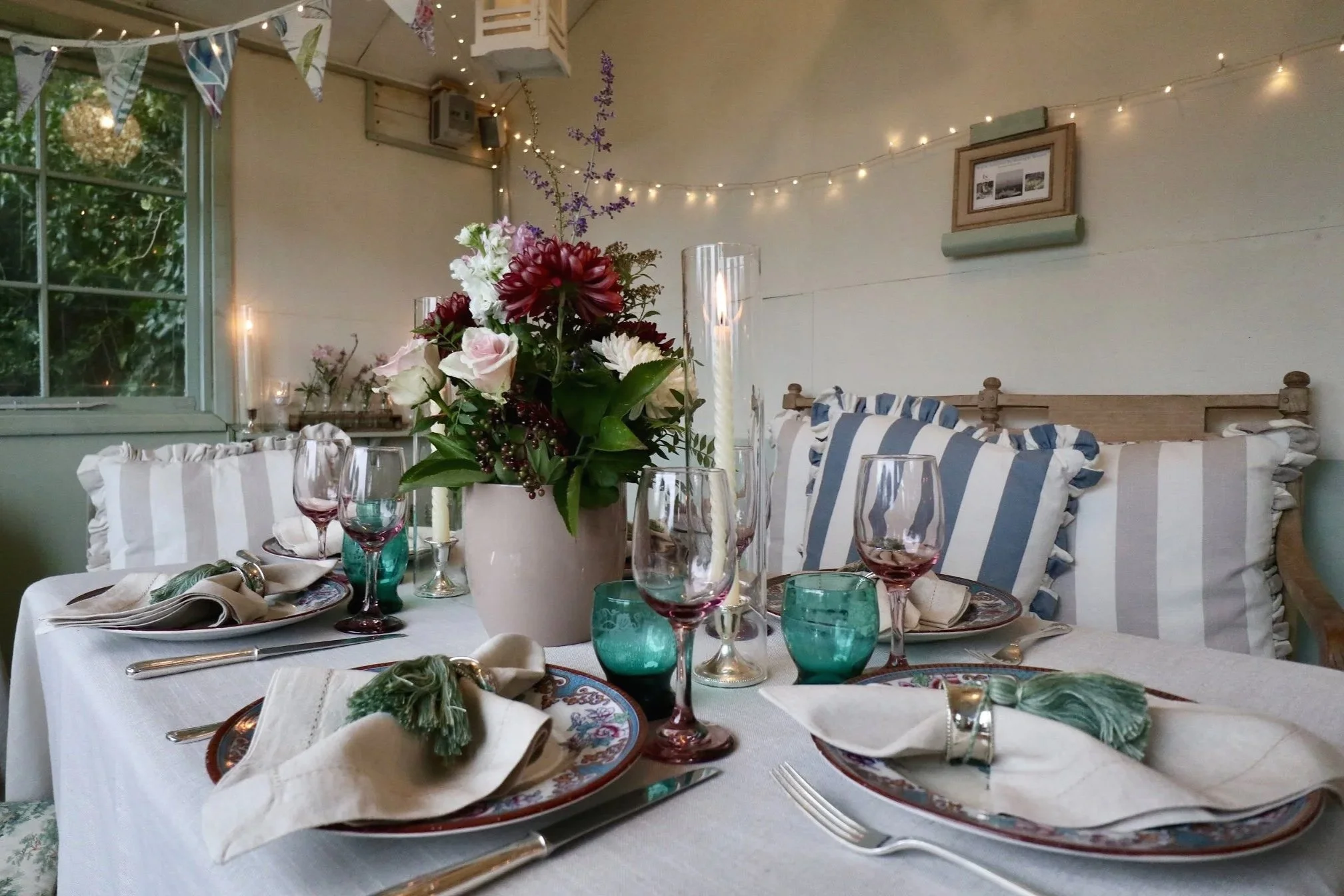 Seasonal floral centrepiece with pink roses, heritage patterned plates, linen napkins and coloured glassware styled by Laura Somborn in Berwick-upon-Tweed.