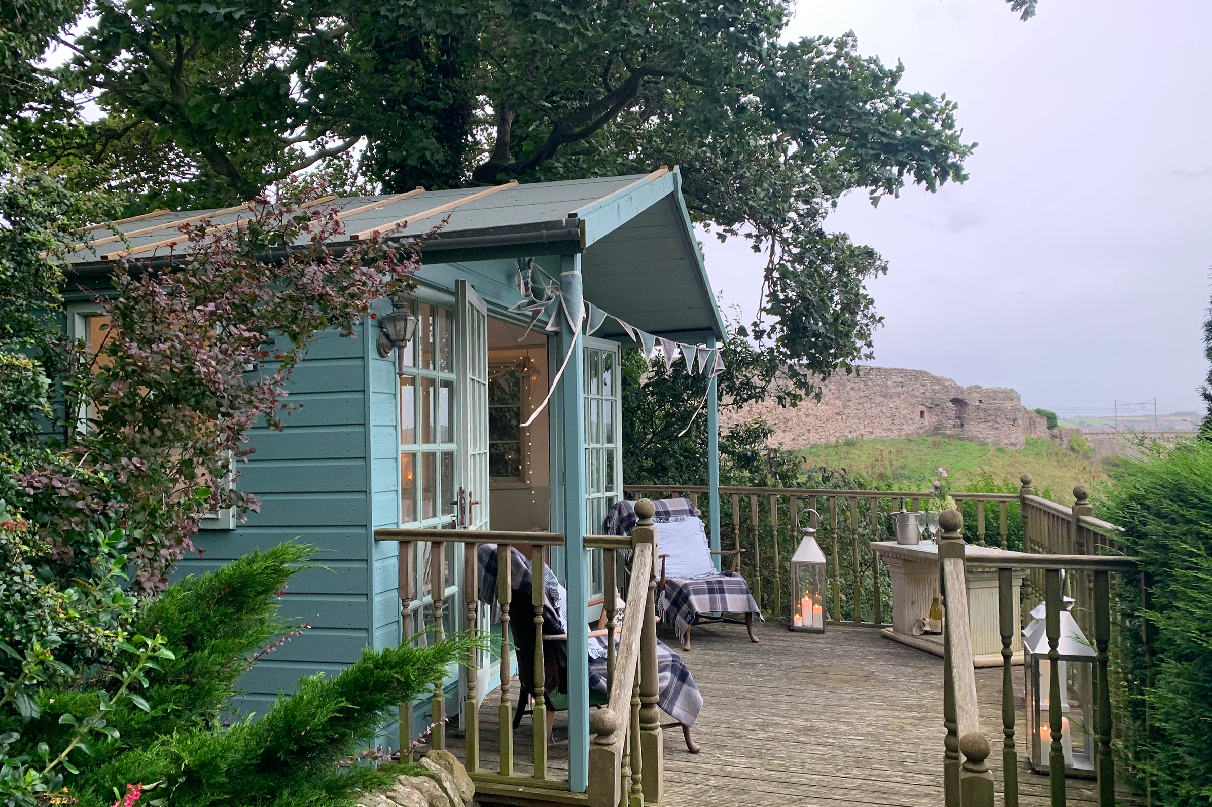 Outdoor gathering space beside a sage-green summerhouse, decorated with lanterns and seeting by Laura Somborn, with views of Berwick Castle and the Royal Border Bridge.