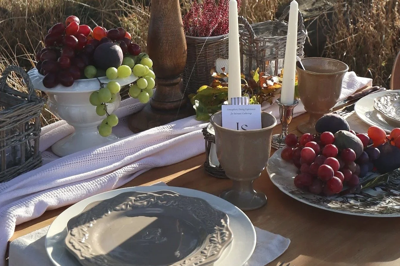 Close-up of a rustic outdoor tablescape with vintage plates, glassware, candles, grapes and plums.