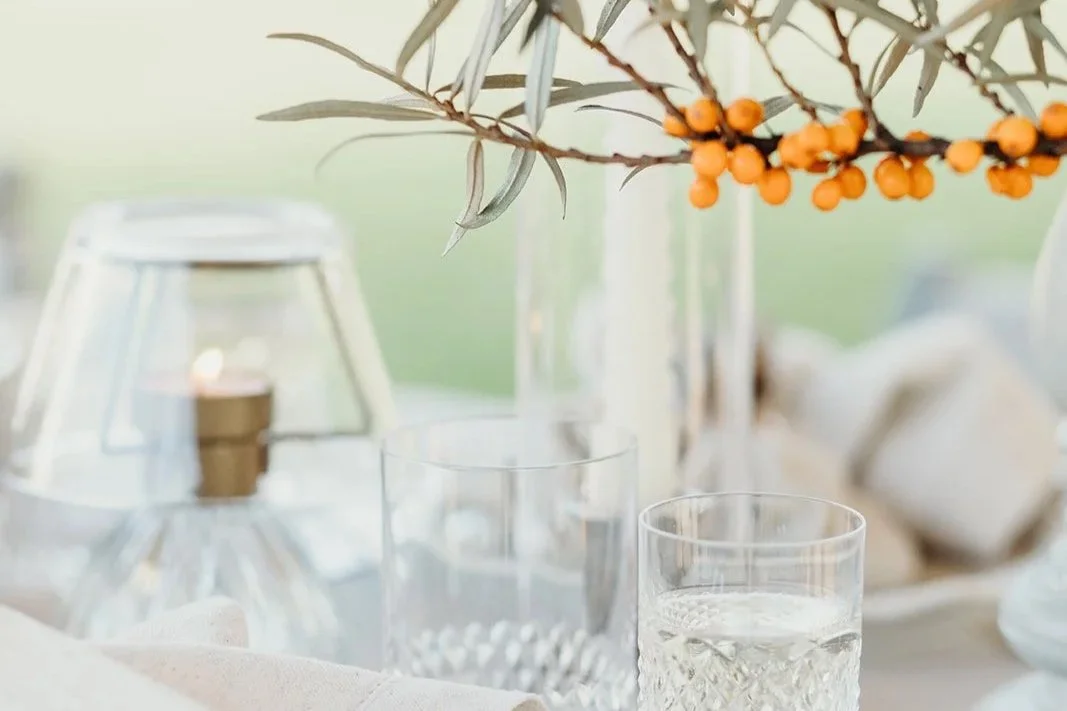 Close-up of an elegant table setting with crystal glassware and pale orange sea buckthorn berries, adding a seasonal accent to Laura Somborn's tablescape design.
