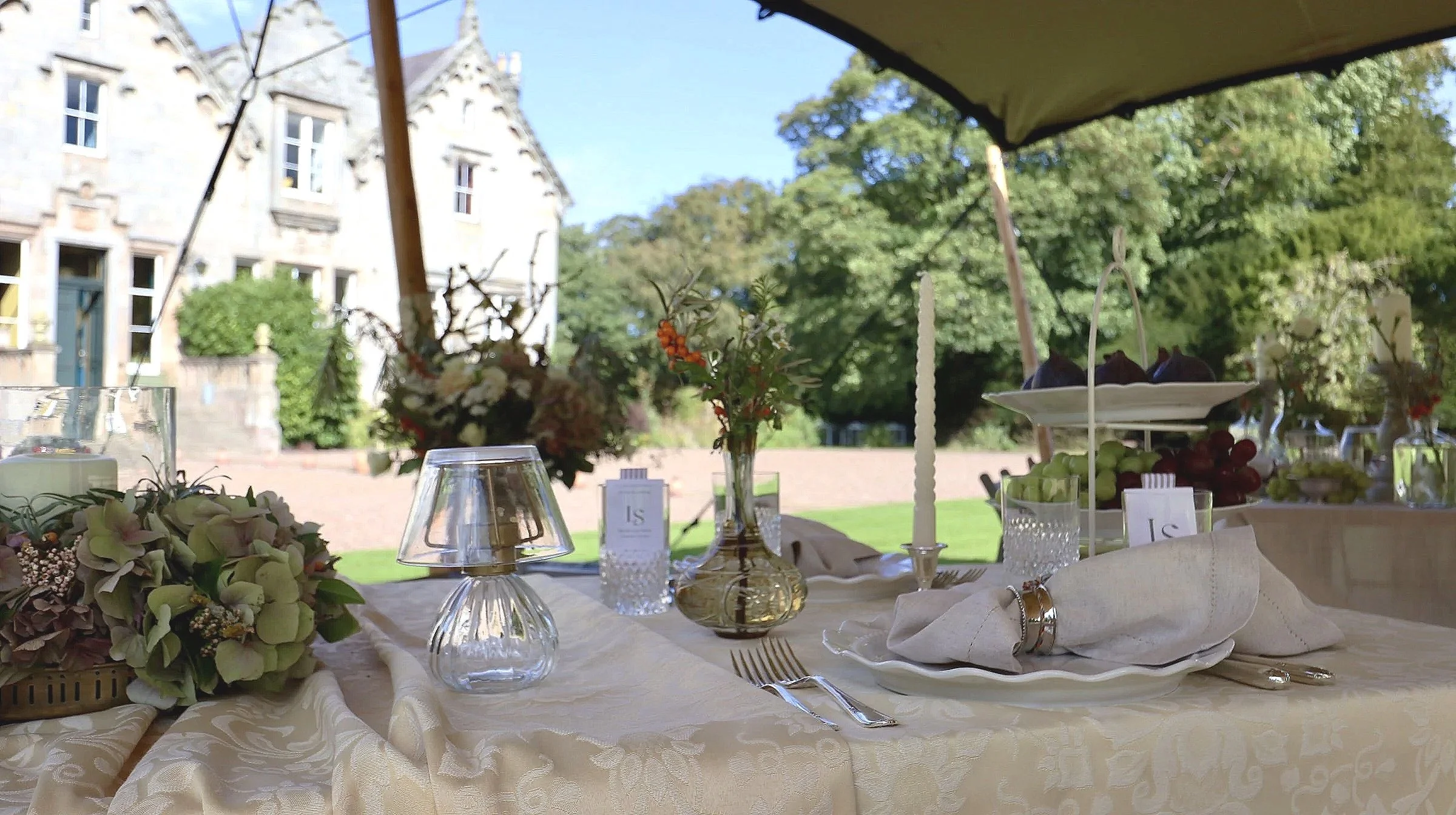 Elegant outdoor tablescape by Laura Somborn at Netherbryres House, featuring pale linens, seasonal flowers, candles and vintage-inspired tableware beneath a stretch tent.