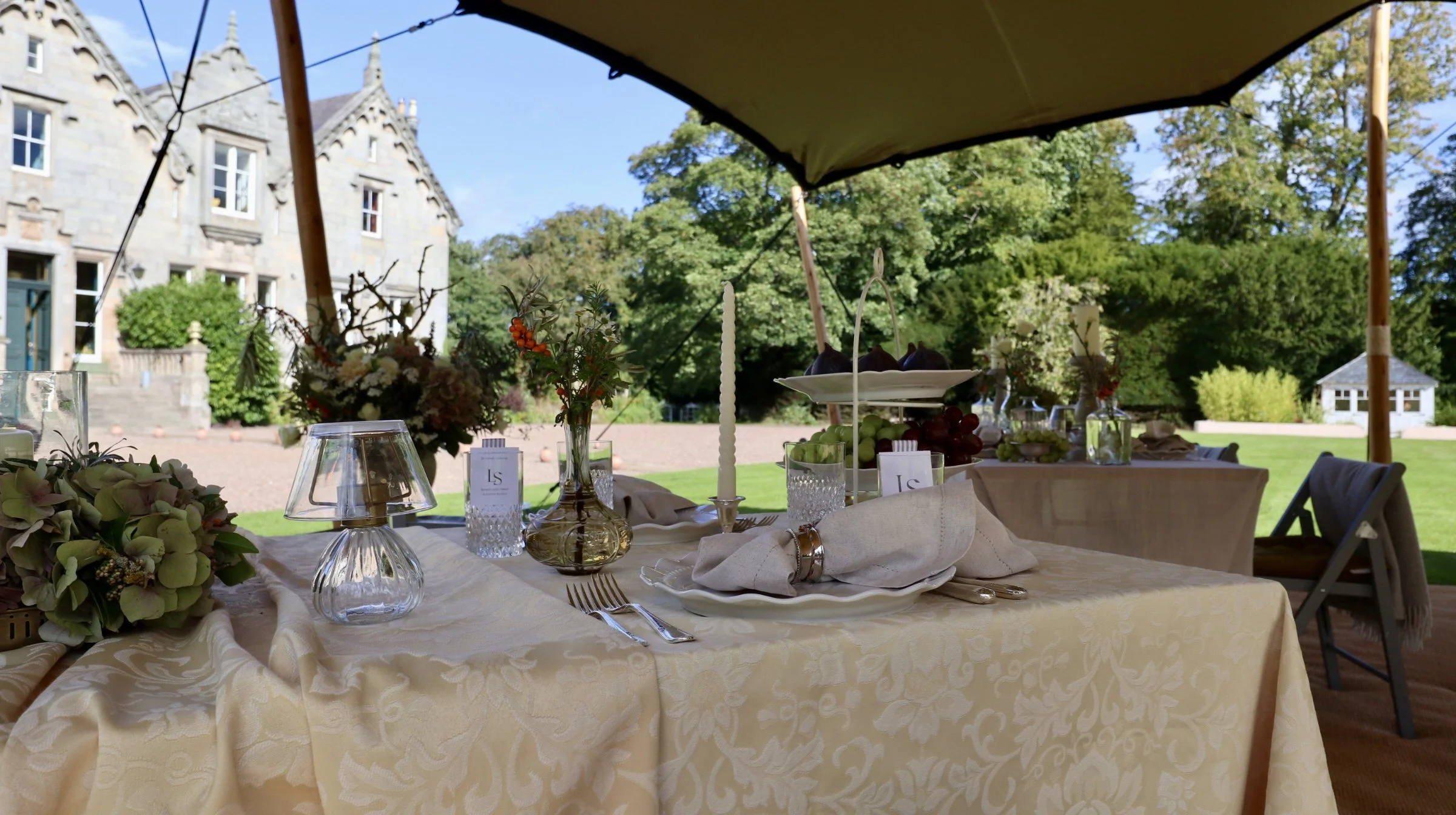Outdoor dining table styled by Laura Somborn beneath a stretch tent in the gardens of Nethetbryres House, with natural textures and understated seasonal details.