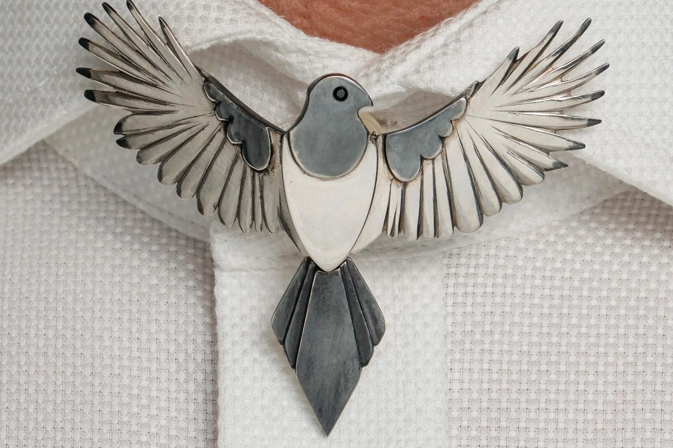 A decorative metal sculpture of a bird with outstretched wings, mounted on a white textured fabric background.