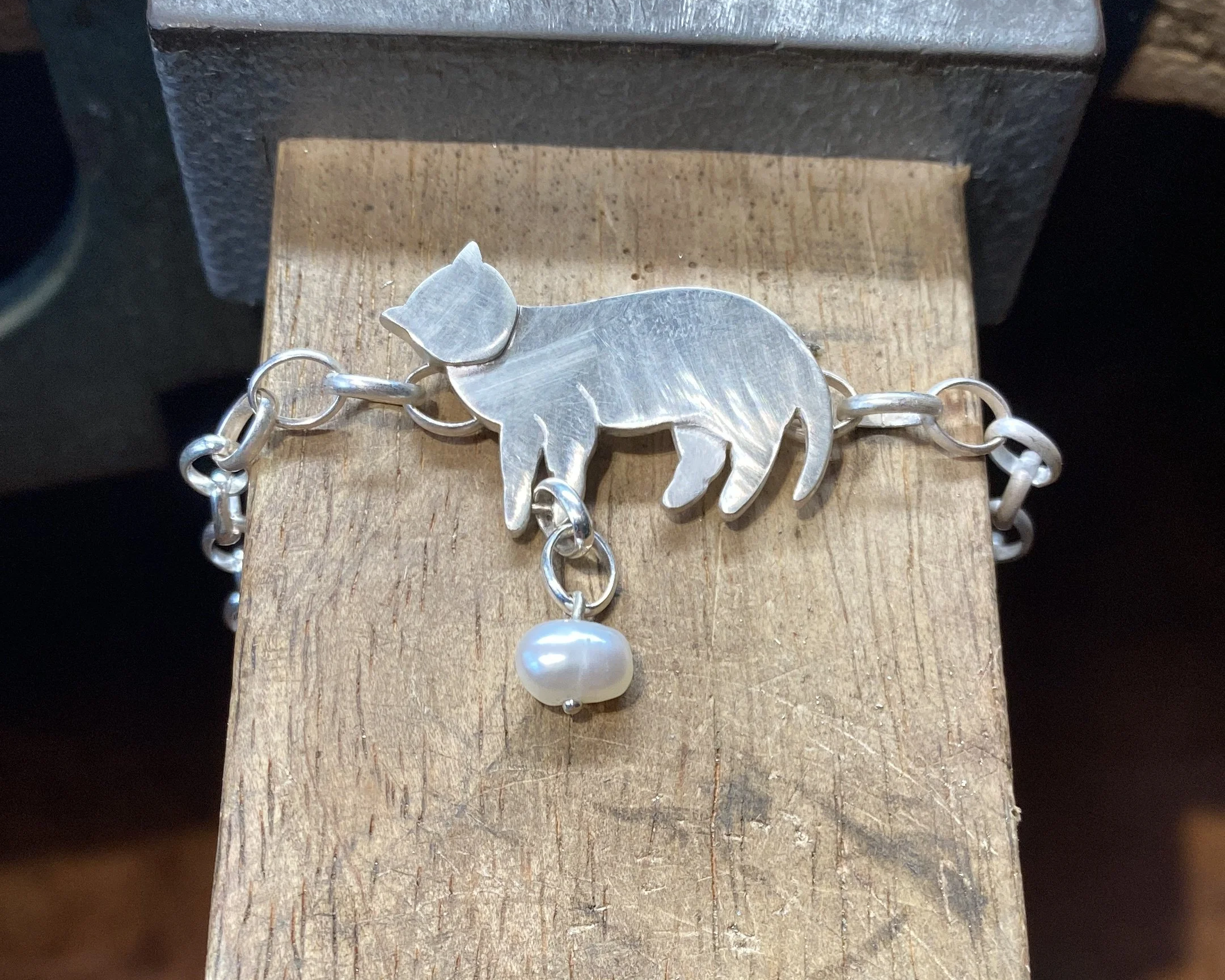 I created the bracelet out of a multitude of different gauge sheet silver and created two matching hidden jumps on the back of the bracelet to hide the chain connections. The drop was attached with a hidden rivet to allow the chain to move freely. Ha