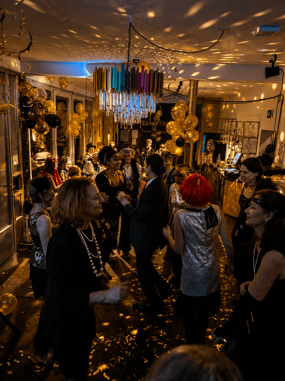 Menschen tanzen und feiern bei einer Party mit goldenen und schwarzen Luftballons, glänzenden Dekorationen und einer Disco-Atmosphäre.