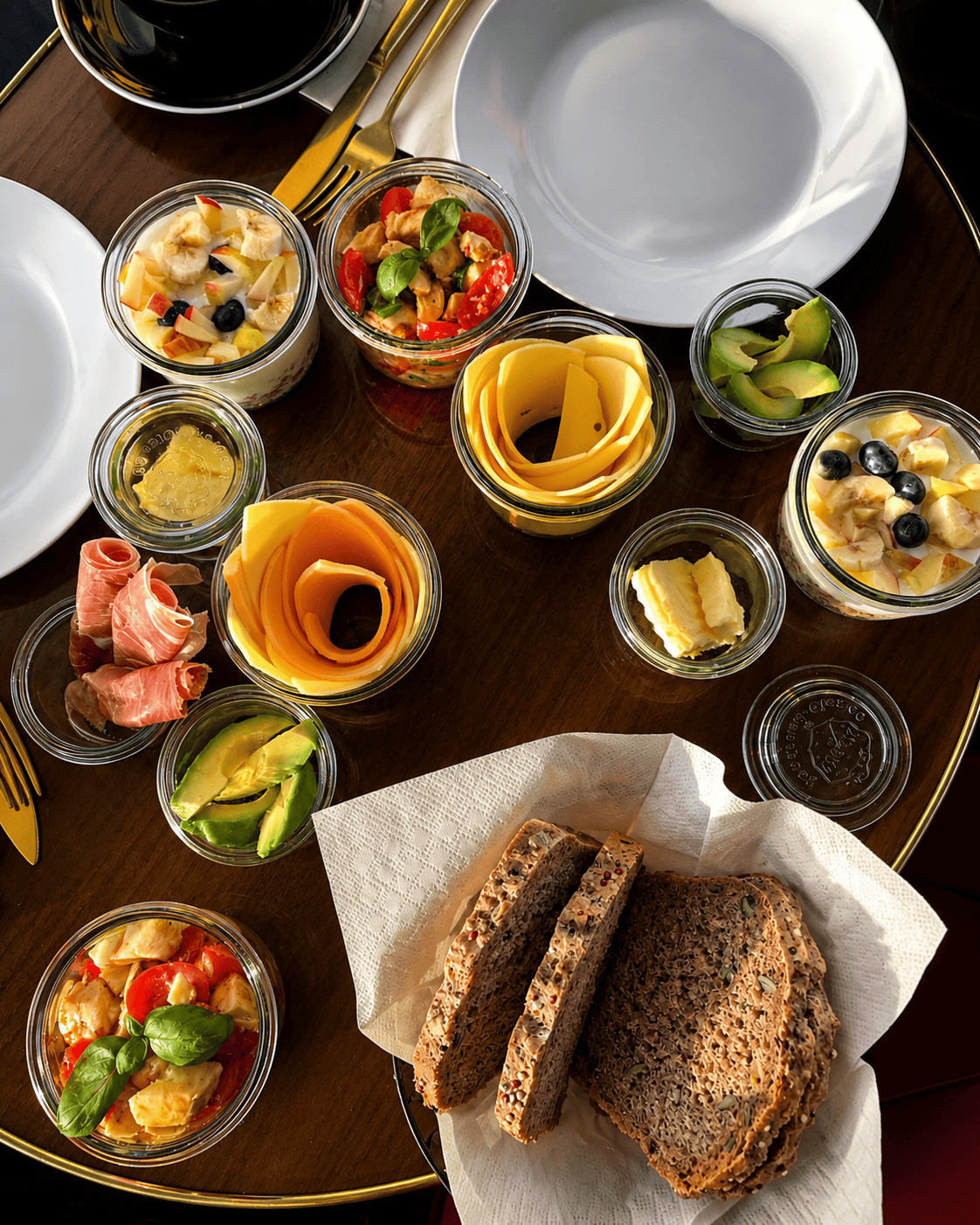 Eine Tischplatte mit verschiedenen Schüsseln, die Käse, Wurst, Oliven, Salate und Vollkornbrot enthalten.