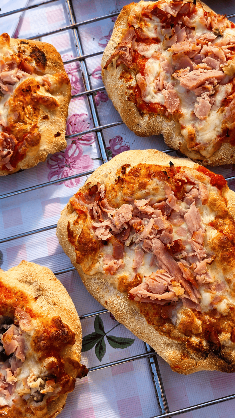 Mehrere kleine Pizzen mit Käse, Schinken und Salami auf einem Gitterrost.