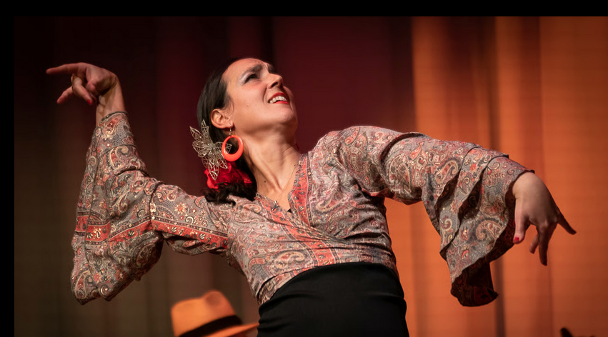 Feierabend im Freien mit einem Flamenco-Tänzerin in einem roten Kleid mit Pailletten, einem Gitarristen im Hintergrund, der singt und Gitarre spielt, bei abendlicher Beleuchtung und festlicher Dekoration.