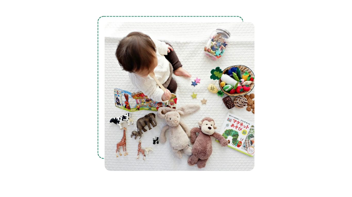 Enfant jouant avec des jouets en peluche, livres, objets en bois, et autres petits jouets colorés, sur une surface blanche.
