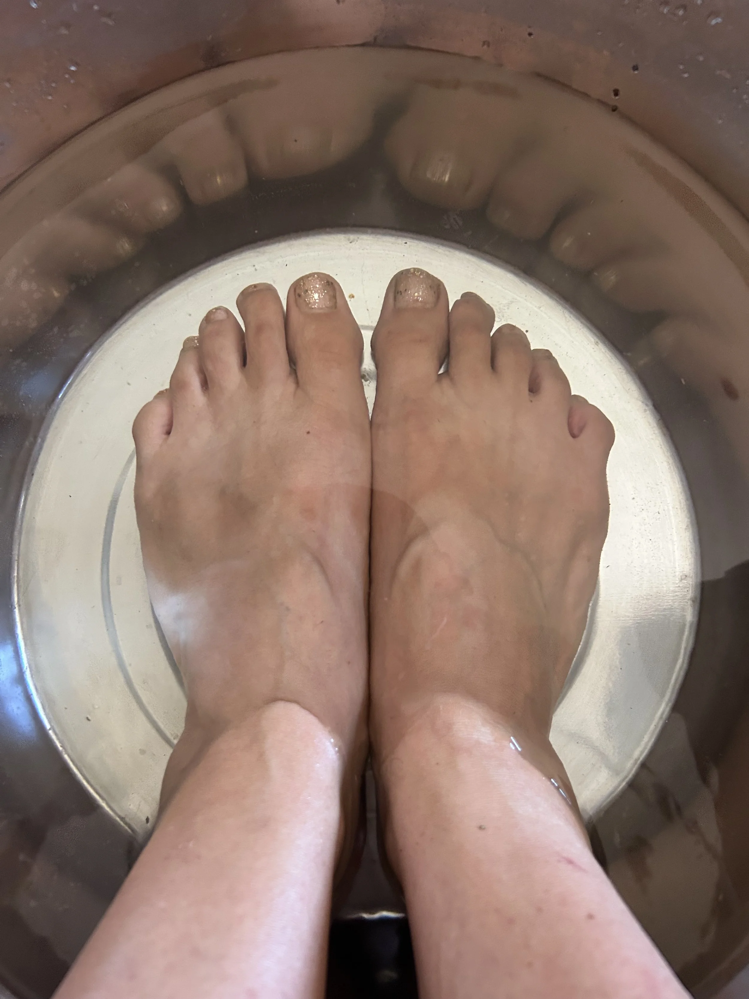 Deux pieds nus en cours de lavage sous l'eau dans une bassine en métal.