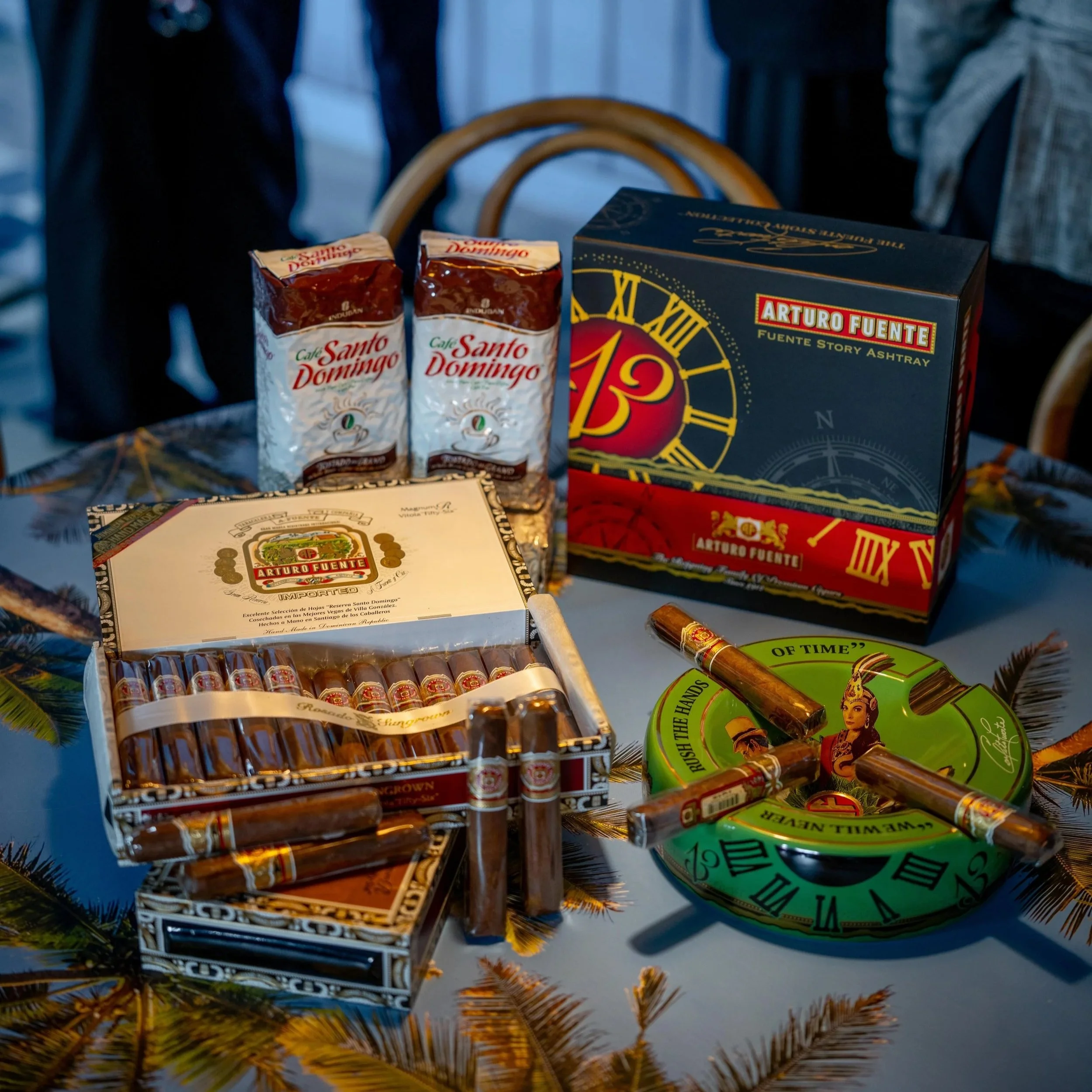 Cigarettes, cigares, et cigares en coffret, ainsi que deux paquets de café Santo Domingo et un jeu de société Arturo Fuente sur une table décorée de branches de sapin.