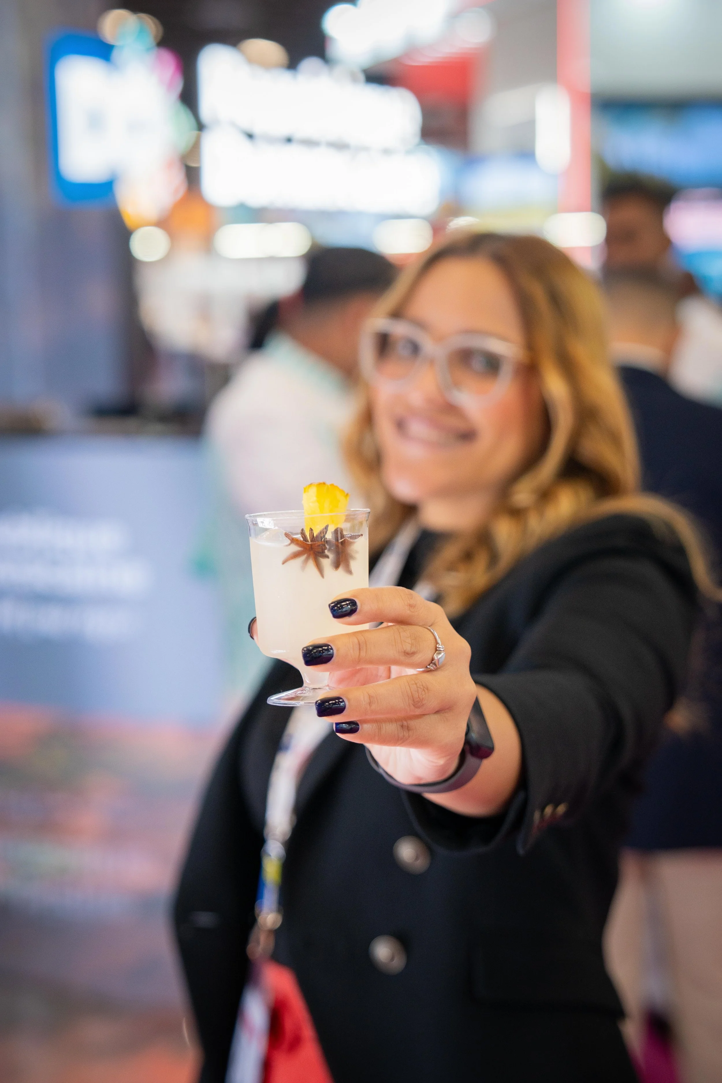 Femme souriante tenant un cocktail décoré avec des étoiles de badiane et un morceau d'ananas dans un lieu animé
