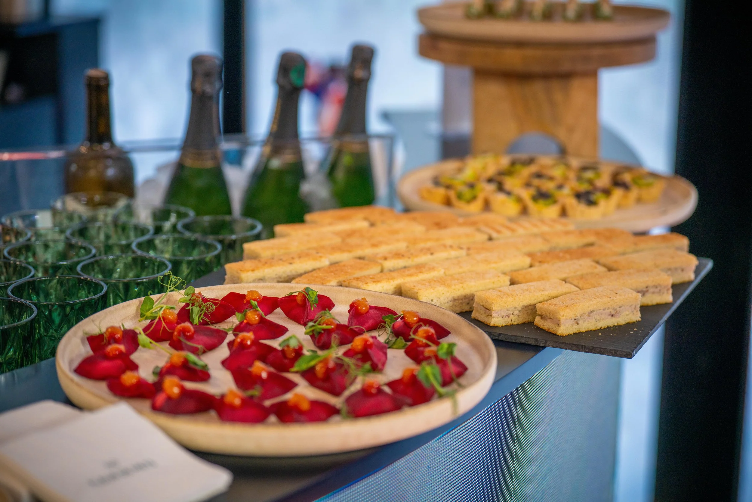 Plateau de sandwichs, entrée à base de betteraves, pizza aux légumes, verres verts, bouteilles de bière.