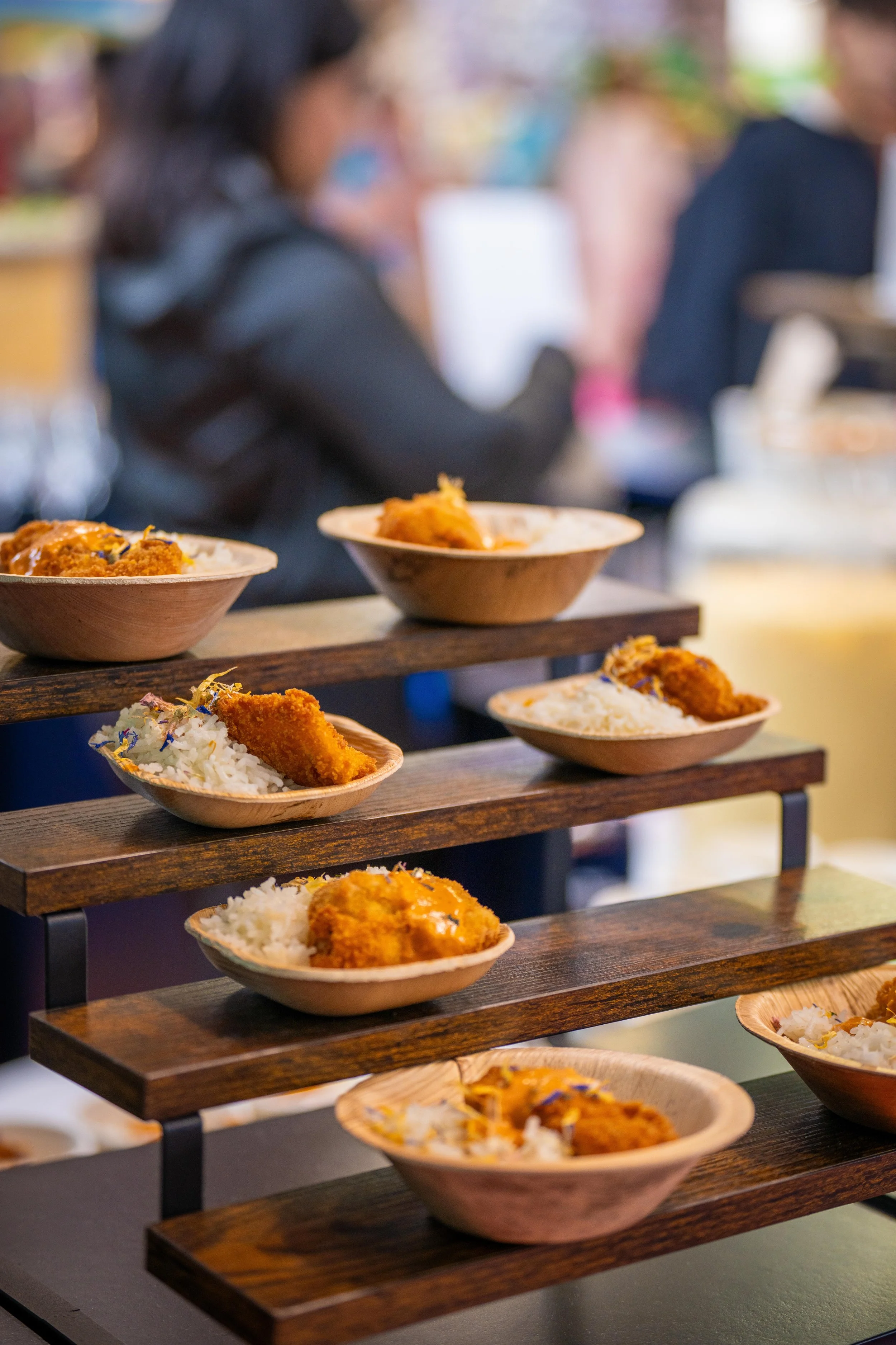 Assortiment de plats indiens à base de riz, curry et fritures présentés dans des bols en bois sur une étagère en bois.
