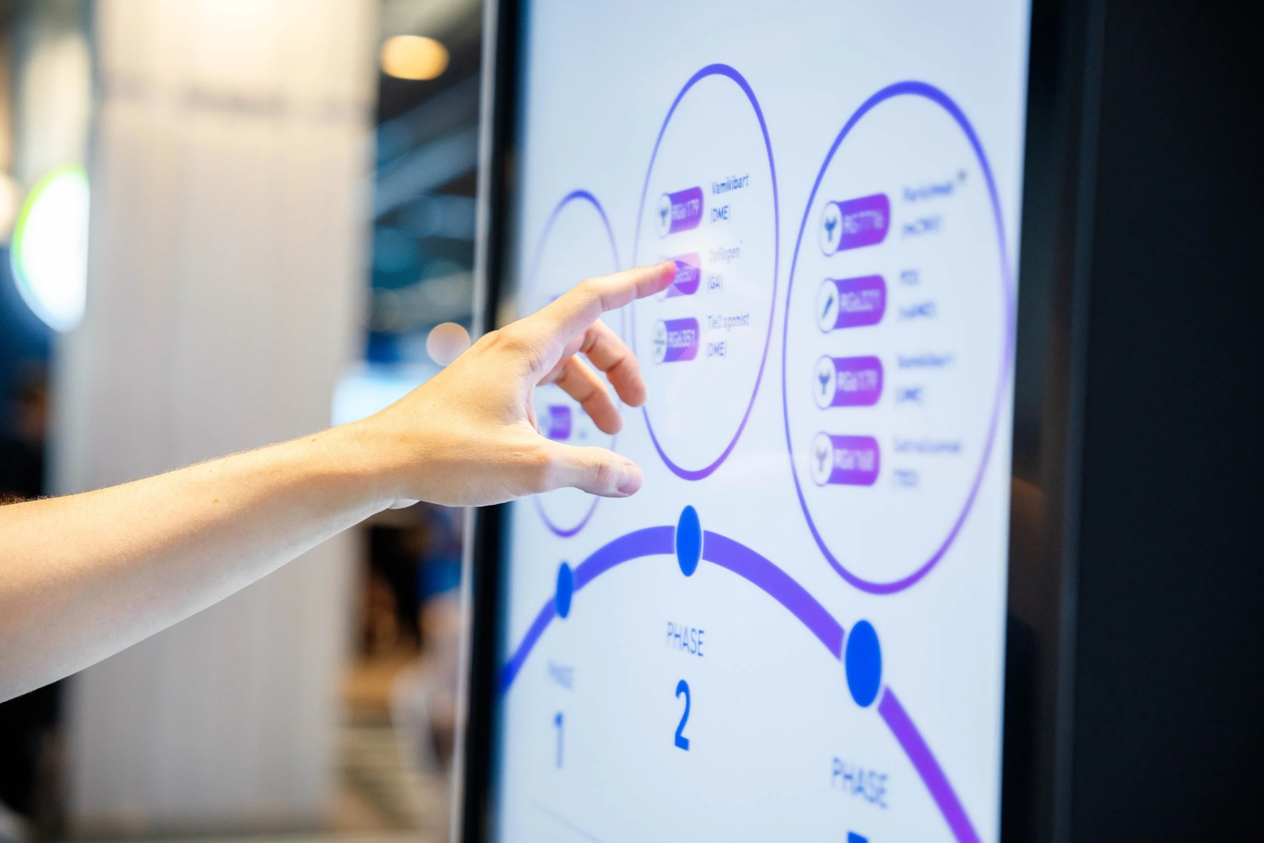 Une main pointant vers un écran numérique affichant un diagramme ou un schéma avec des textes et des cercles colorés en violet et blanc.