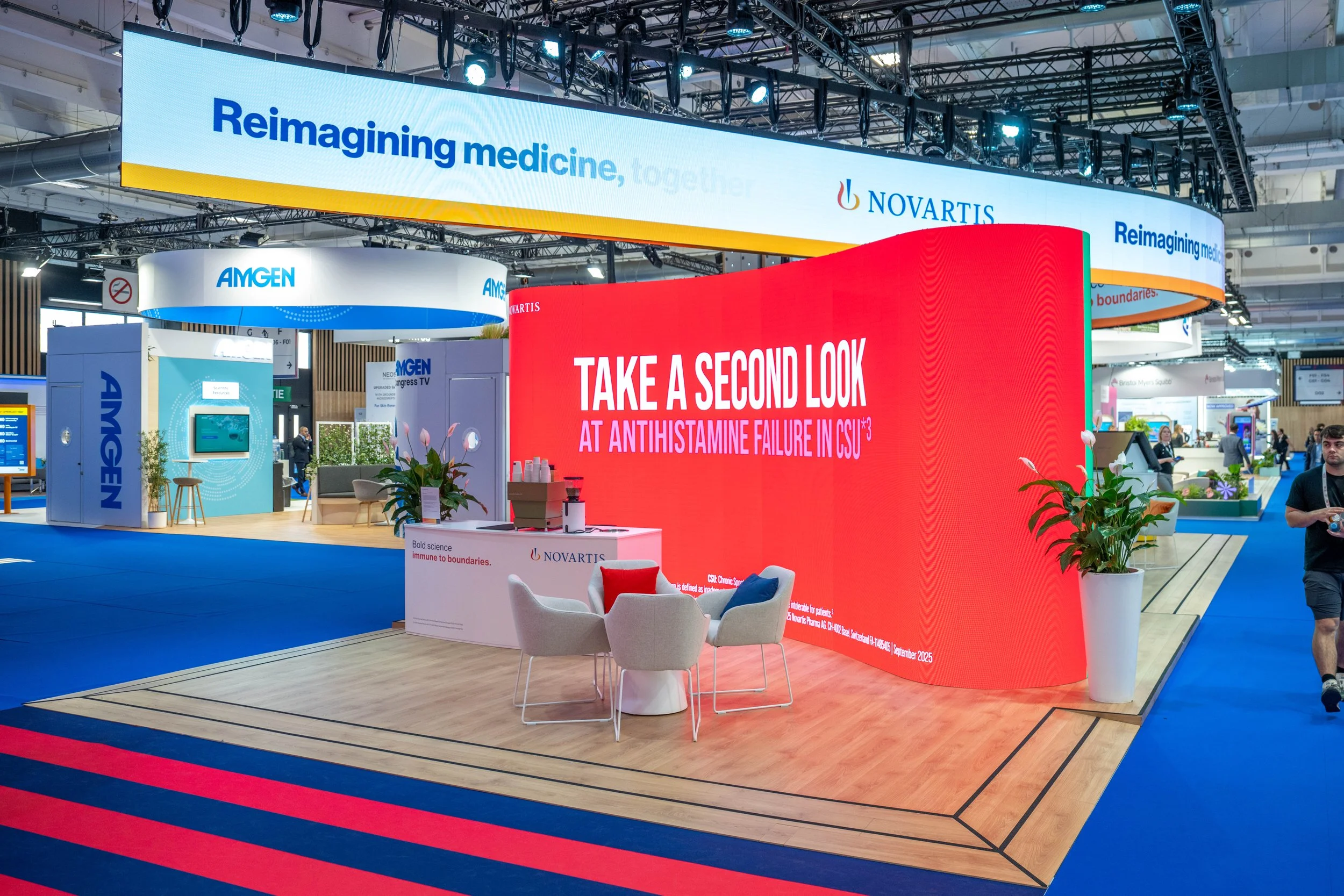 Exposition médicale avec un grand écran rouge affichant le message 'Take a second look at antihistamine failure in CSU' et un autre écran bleu avec le texte 'Reimagining medicine'.