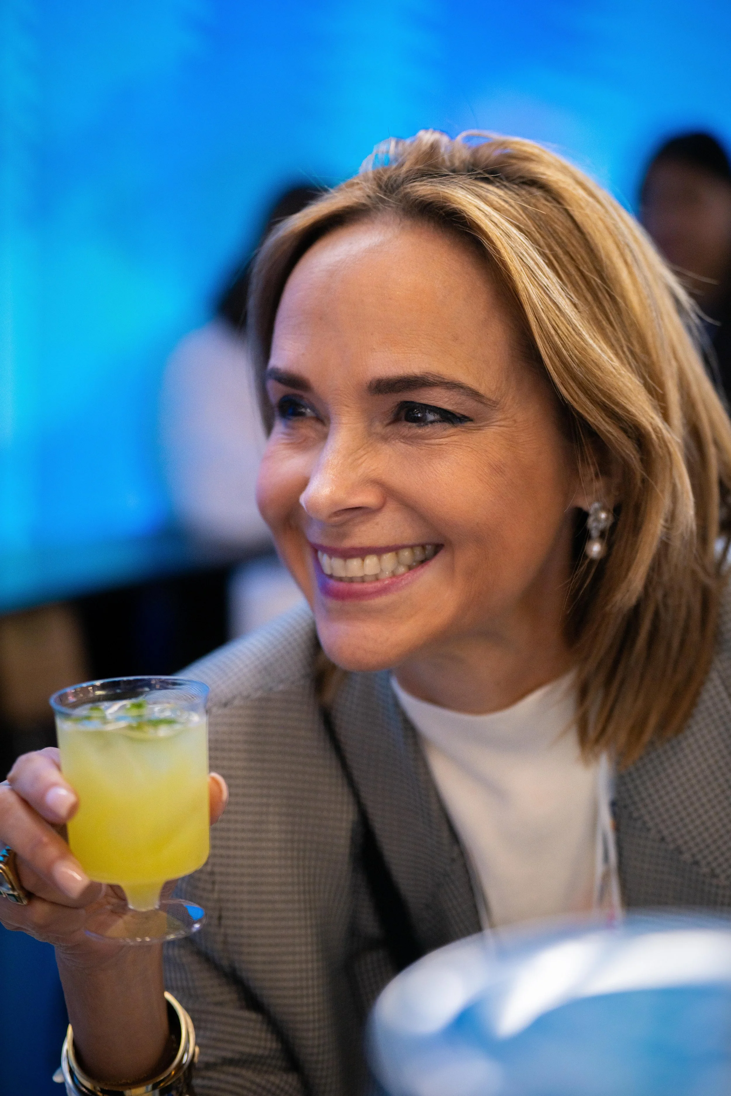 Une femme souriante tenant un verre de cocktail jaune lors d'un événement social.
