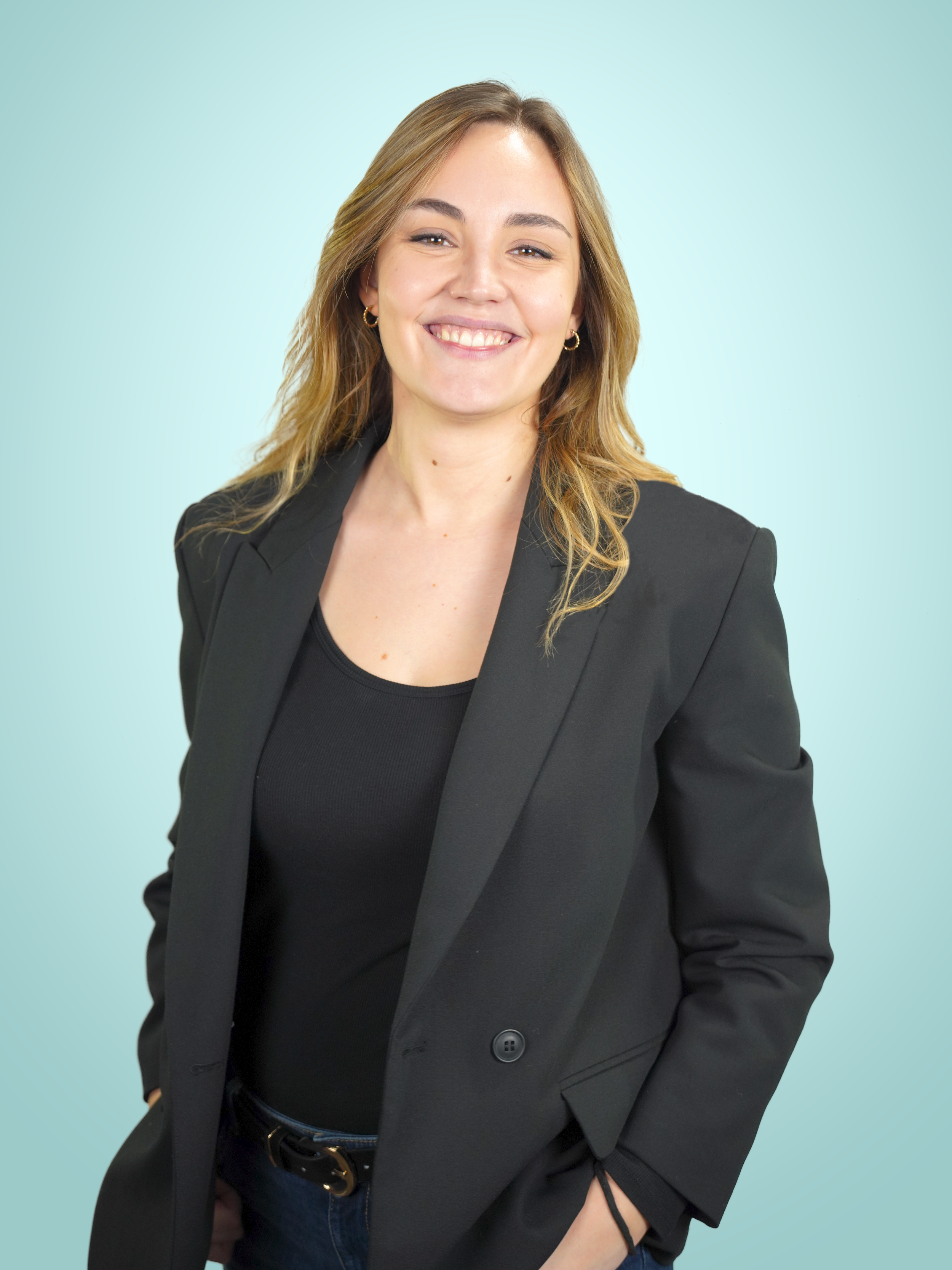 Une femme souriante portant un tailleur noir sur un fond bleu clair.