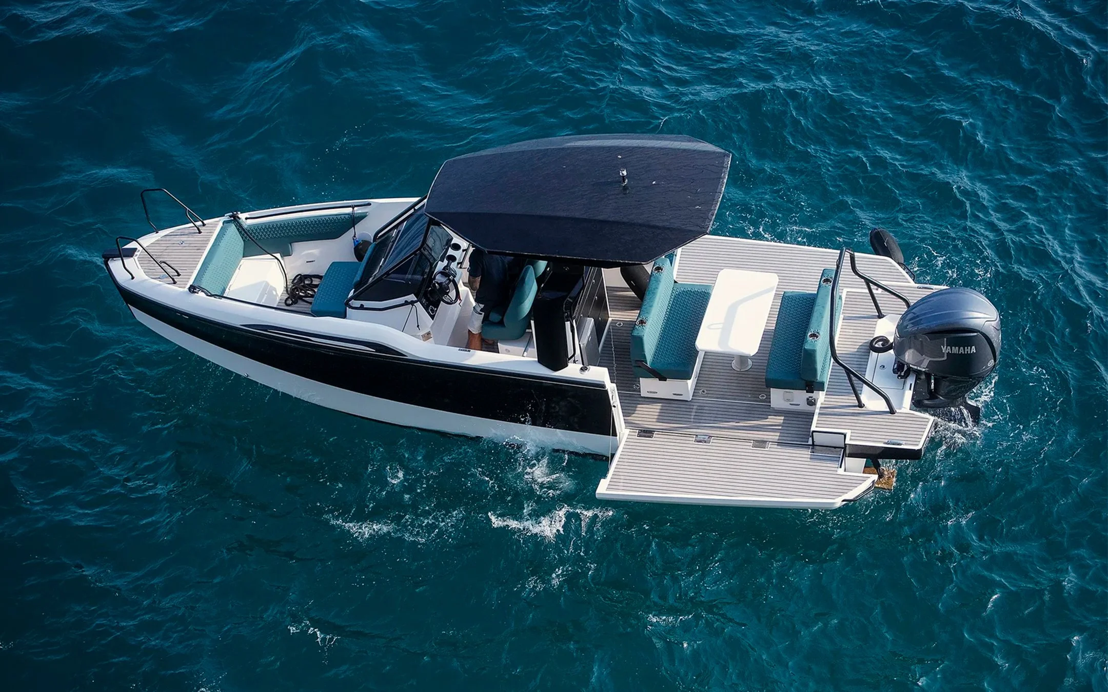 Aerial view of a modern motorboat with a black canopy and Yamaha outboard motor, floating on ocean water.